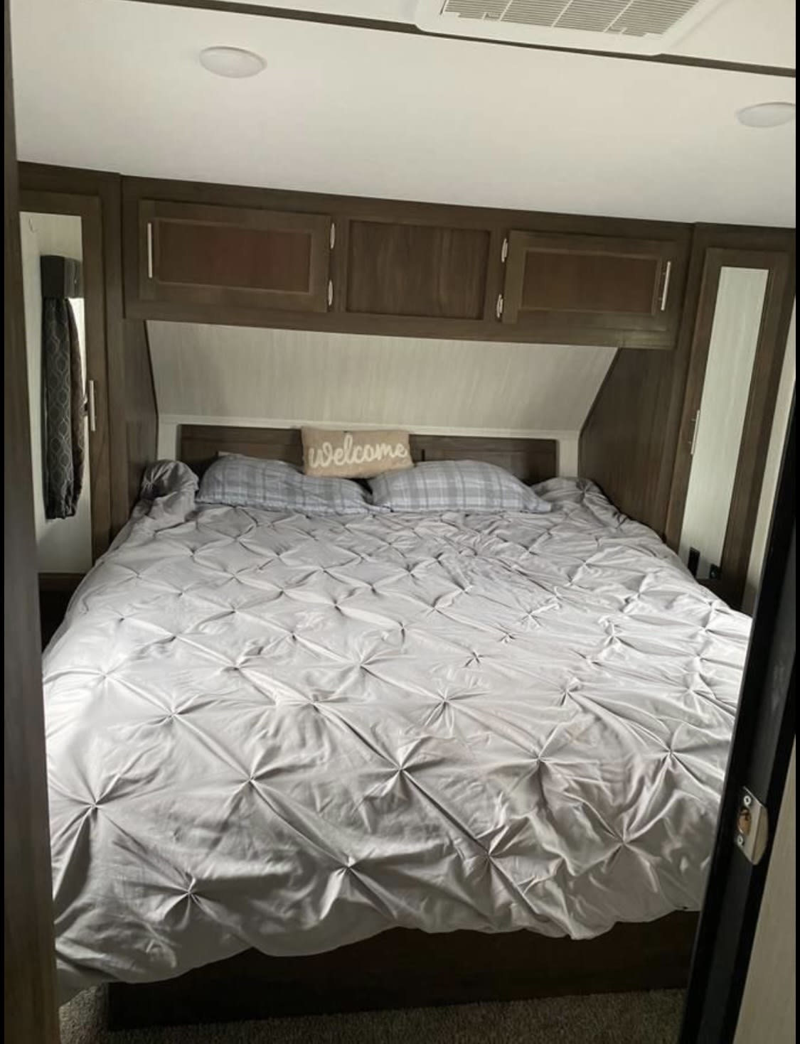 Inviting RV rental bedroom with a large bed, grey comforter, "Welcome" pillow, and overhead storage.. Forest River Wolf Pack 2019