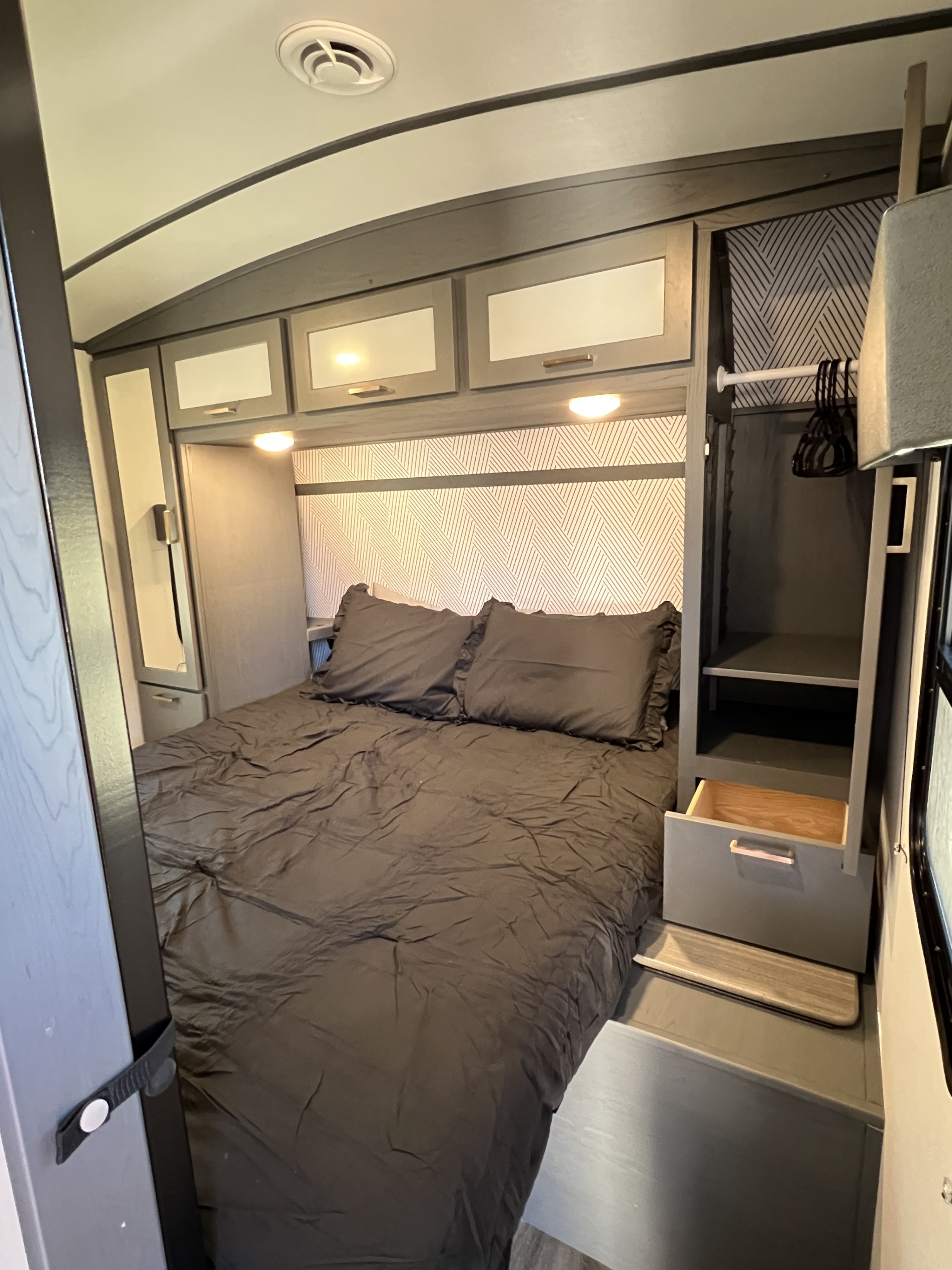 Modern RV rental bedroom featuring dark bedding, overhead cabinets, and built-in storage for comfortable travel.. Keystone RV Bullet Ultra Lite 2024