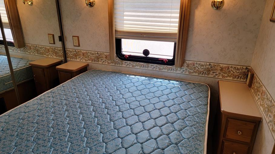 Inside an RV rental bedroom: features a comfortable blue mattress, window, and built-in nightstands for travelers.. Winnebago Adventurer 1999