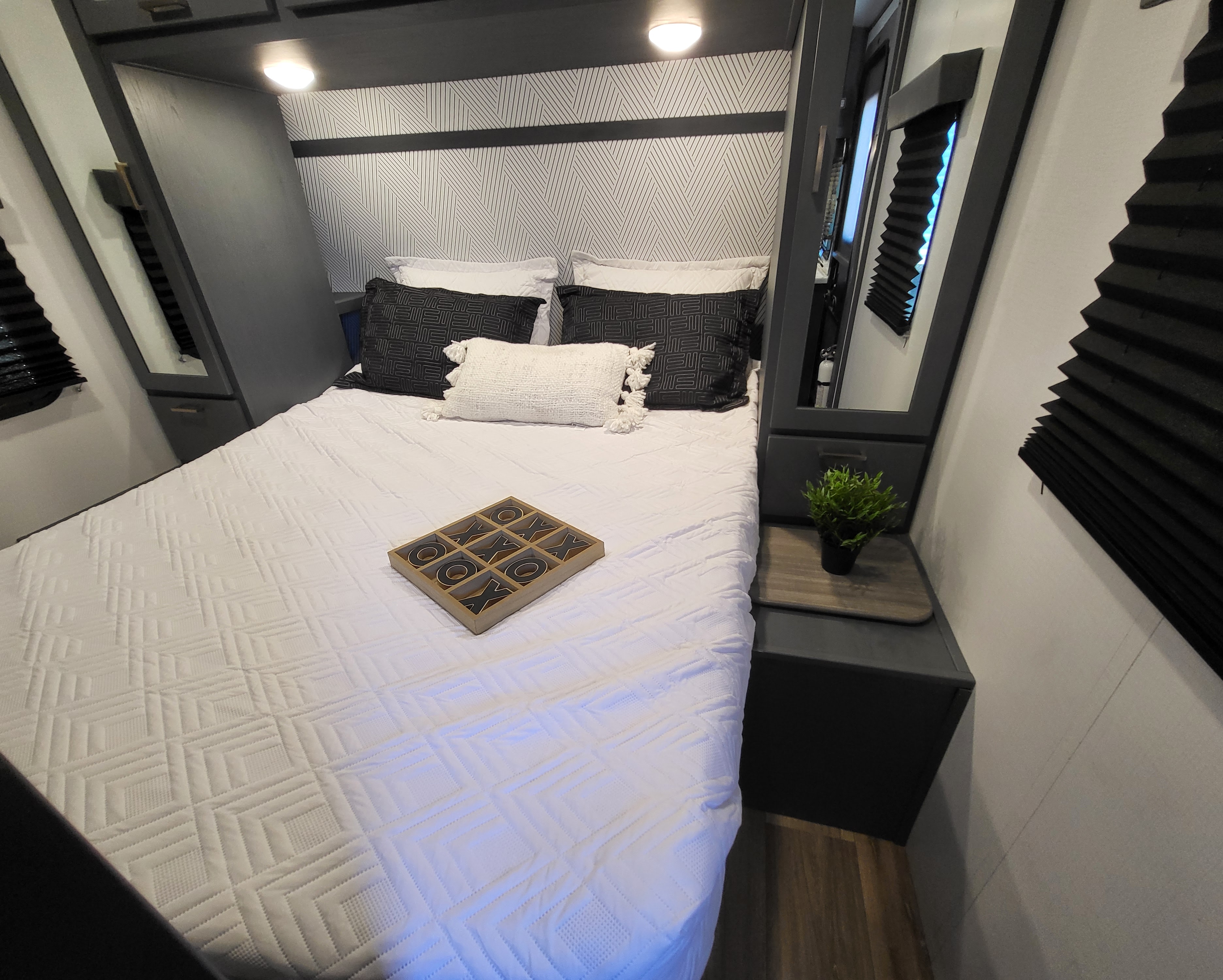 Modern RV rental bedroom with patterned walls, comfy bed, black/white bedding, smart storage, and side table.. Keystone RV Bullet Ultra Lite 2023