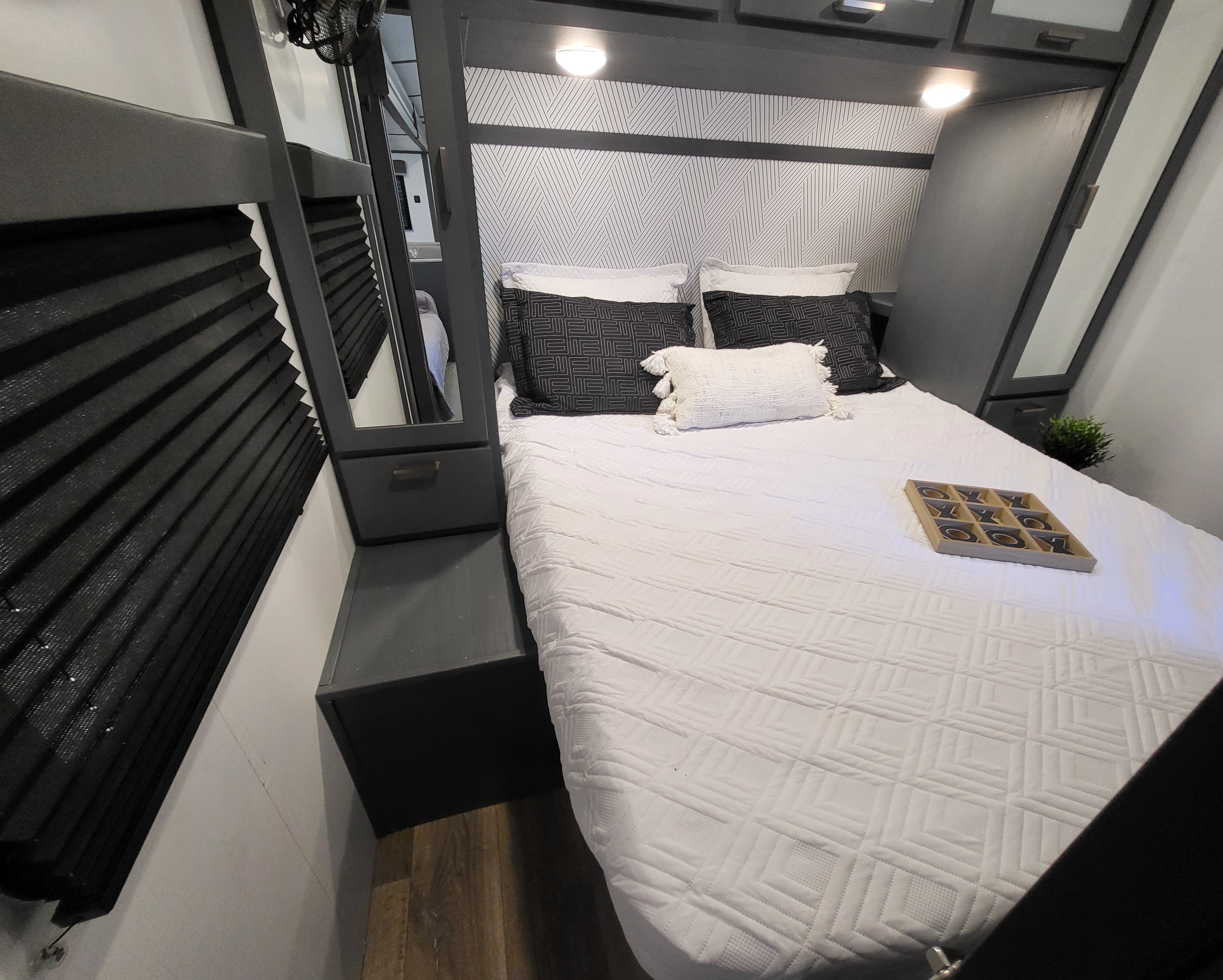 Experience comfort in this RV rental bedroom with dark modern decor, geometric headboard, and plush bedding, complete with a tic-tac-toe game.. Keystone RV Bullet Ultra Lite 2023