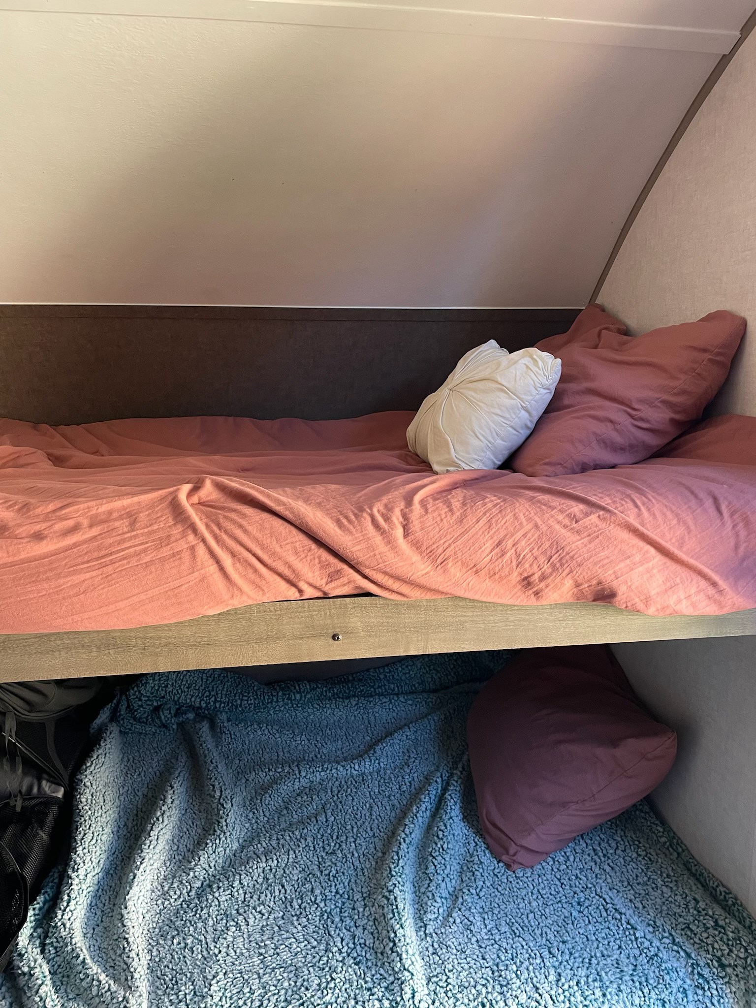 RV rental interior featuring cozy bunk beds. Top bunk has pink bedding; bottom has blue textured blanket and dark pillow.. R-Pod Hood River Edition 2017
