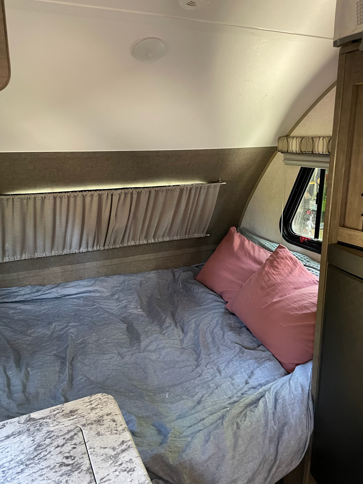 Cozy RV rental bed with blue sheet and pink pillows, providing a comfortable sleeping area with a window.. R-Pod Hood River Edition 2017