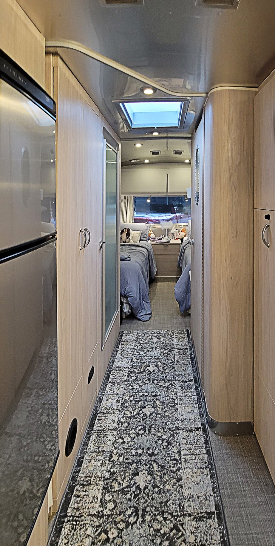 A bright rv rental interior: A modern galley with a rug leads to a bedroom featuring two comfortable twin beds.. Airstream Globetrotter 2022