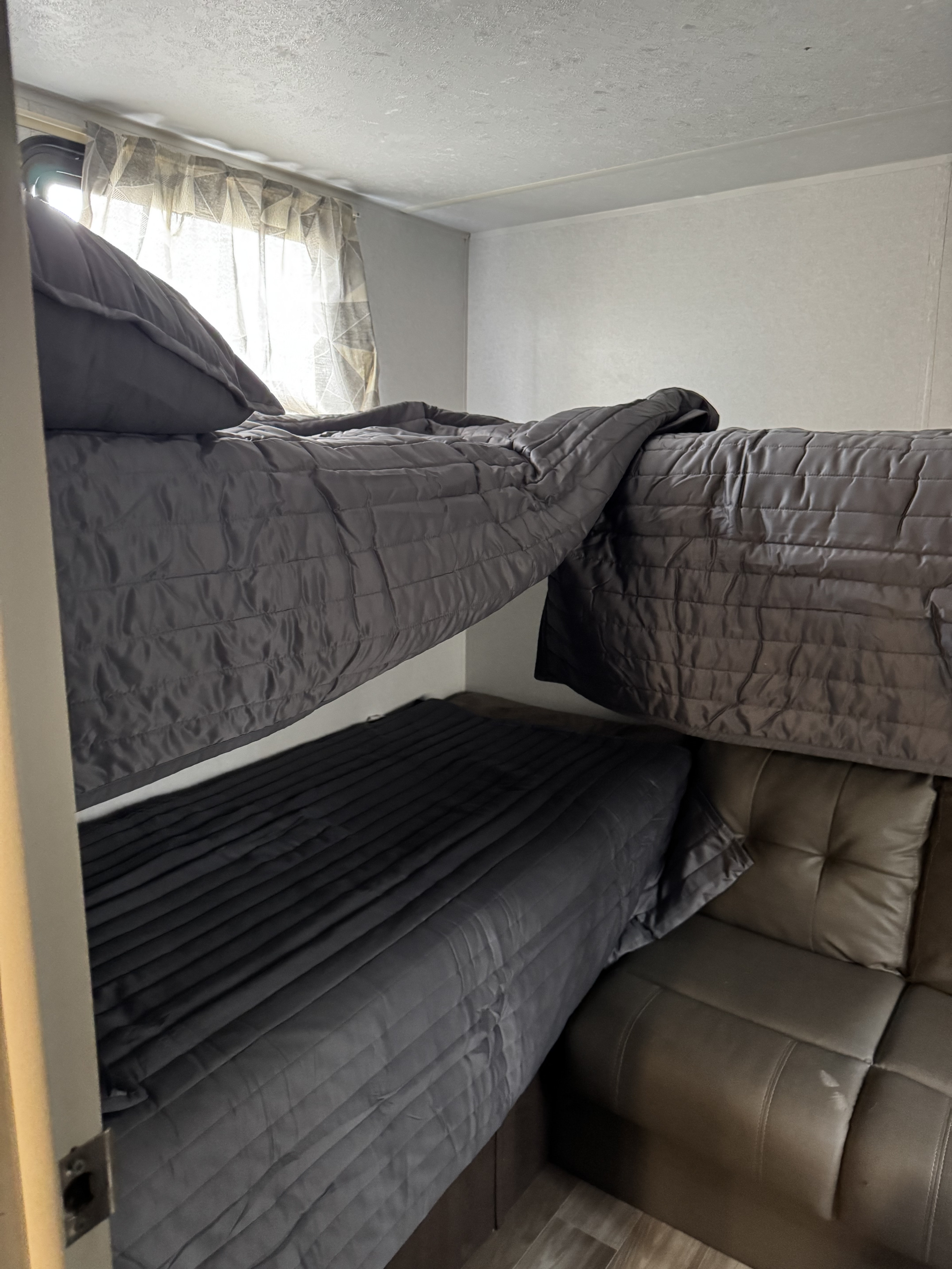 RV rental showing snug dark grey bunk beds on left, with a comfortable leather-look couch on the right.. Forest River Salem FSX 2019