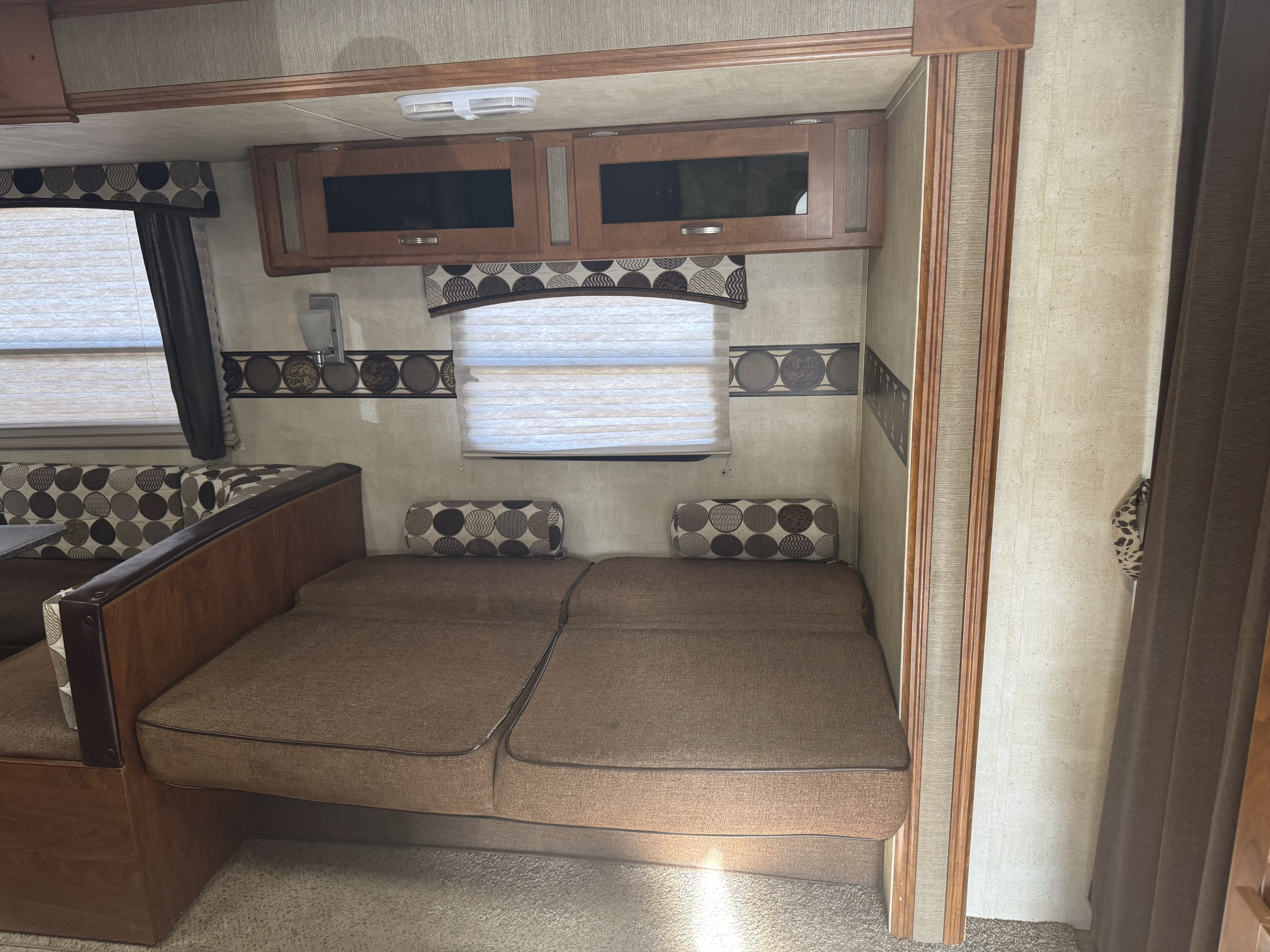 Inside this rv rental, you see a cozy living space with convertible sofas, overhead storage, and patterned decor.. Keystone RV Passport Grand Touring 2014