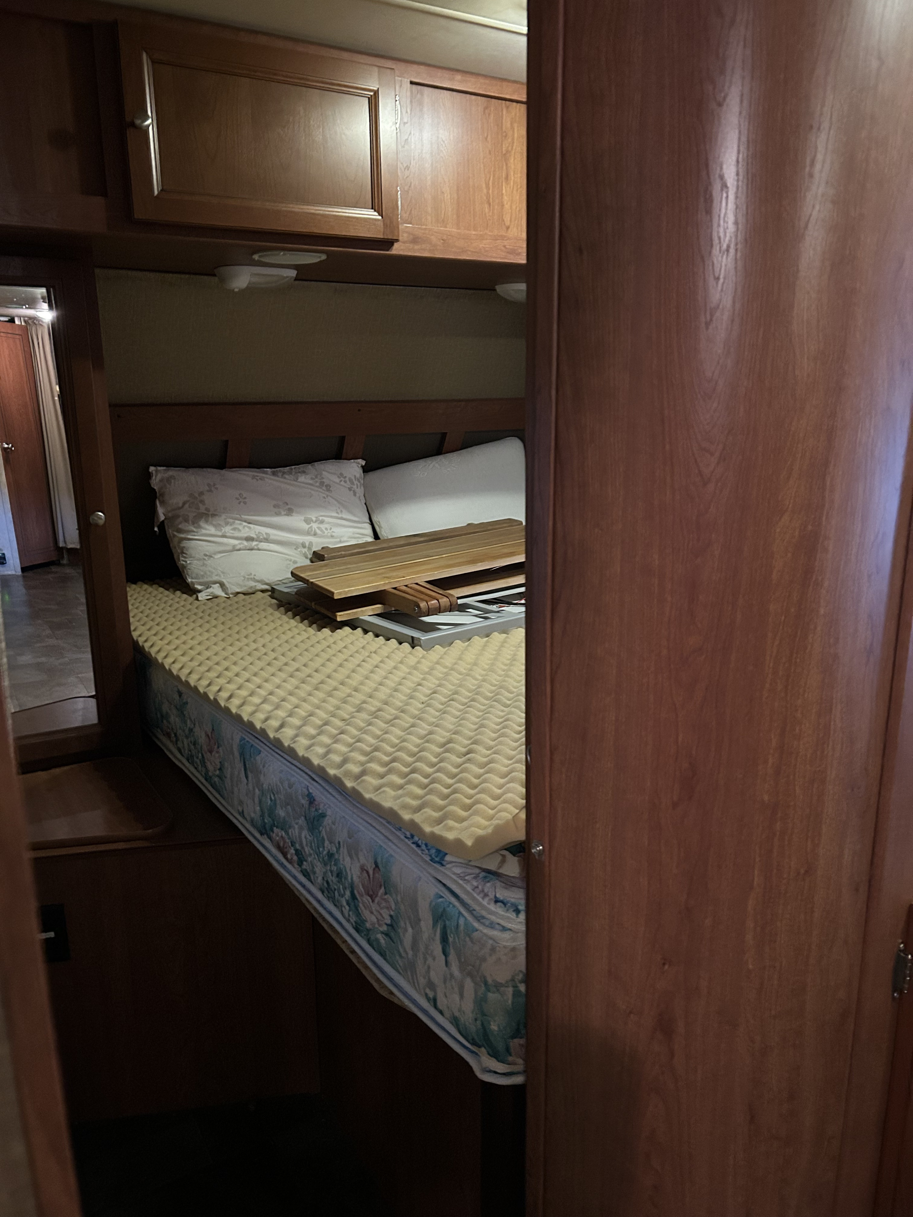 RV rental bedroom: a bed with a foam topper, pillows, and wooden cabinets above. A functional and cozy interior space.. Dutchmen Coleman Explorer 2013