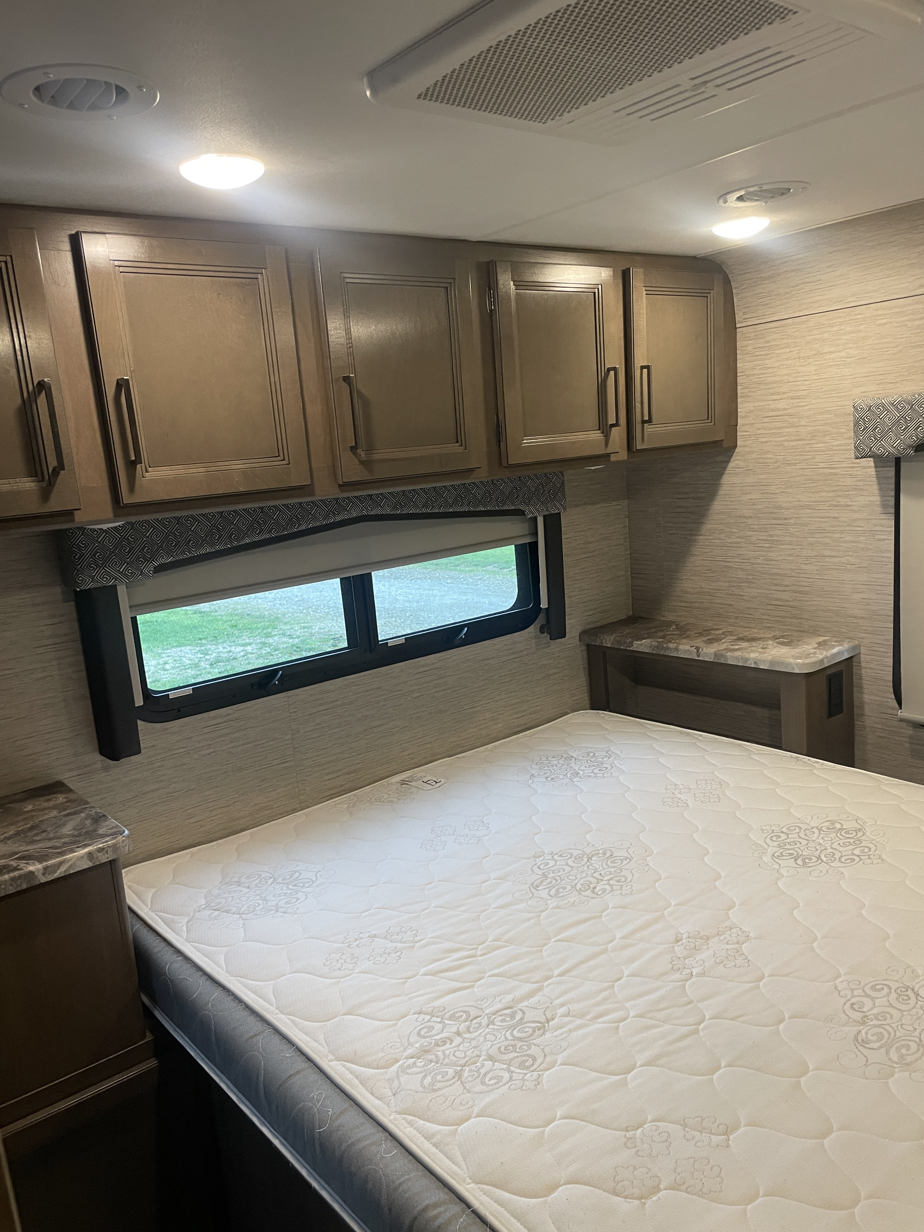 Comfortable RV rental bedroom featuring a bed, overhead storage, and a window with an outdoor view.. Thor Chateau 2022