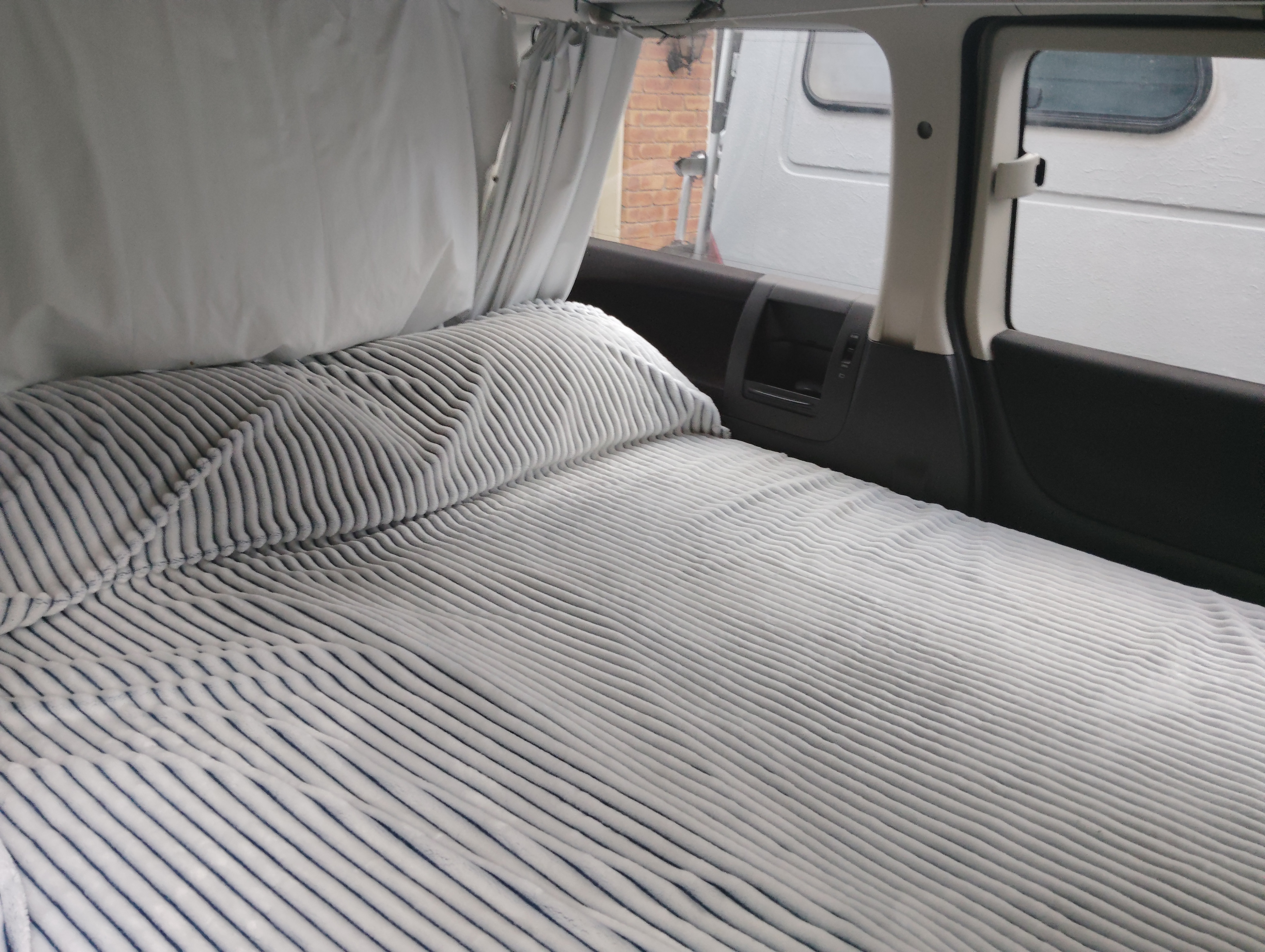 Cozy RV rental bed setup with soft, striped bedding. Perfect for comfortable travel and van life adventures.. Nissan Elgrand 2005