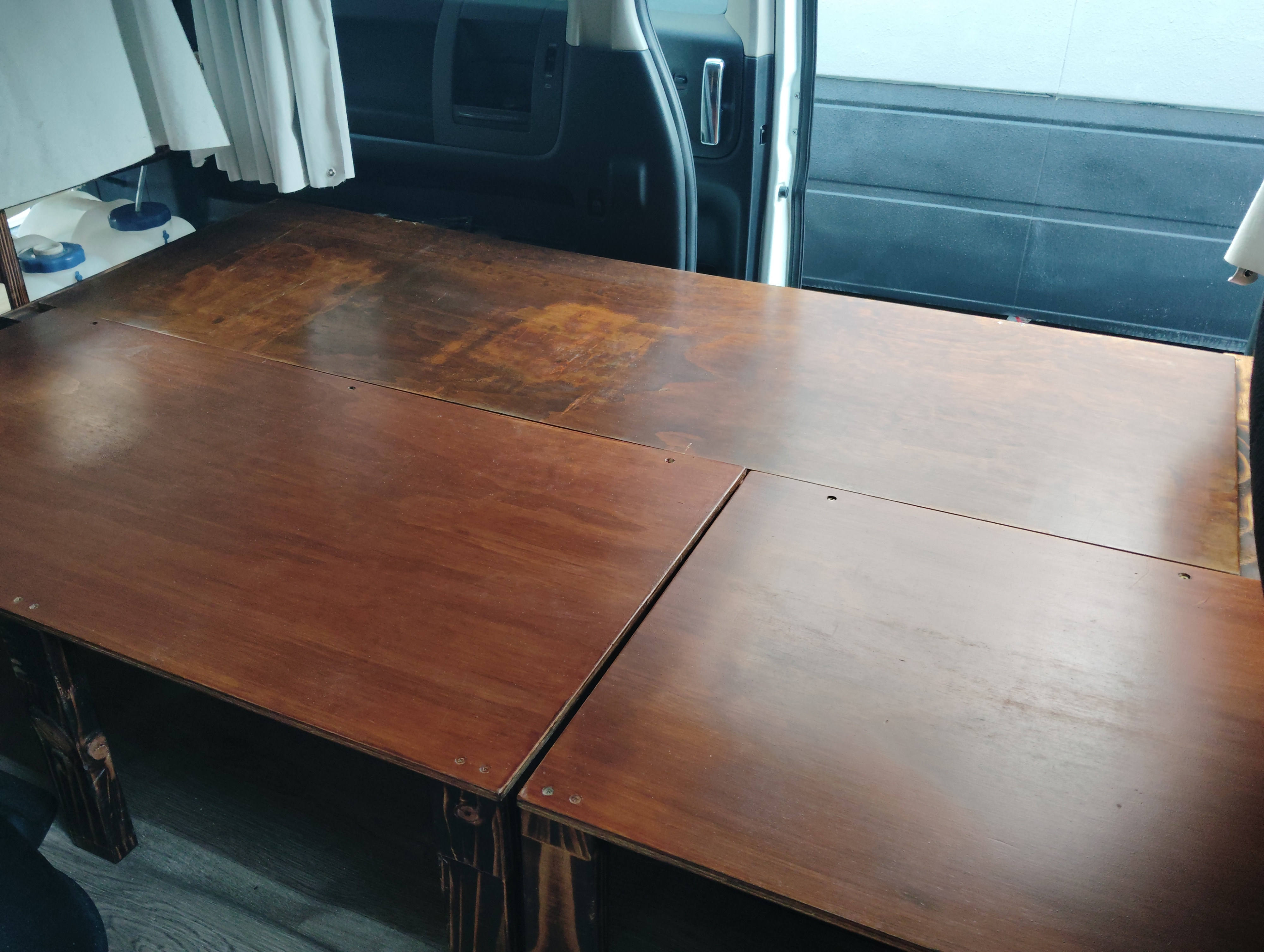 Durable wooden bed platform in an RV rental's cozy interior, featuring storage containers and open door for ventilation.. Nissan Elgrand 2005