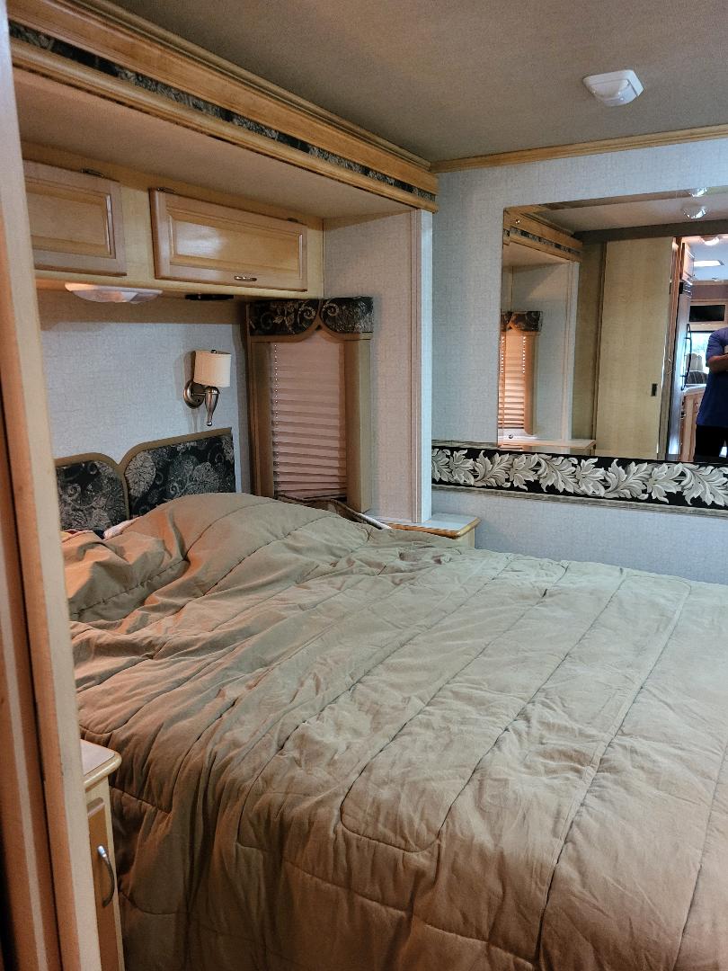 Plush bed in an RV rental bedroom with wood trim, wall sconce, and mirrored wall.. Southwind Southwind Motorhome 2005