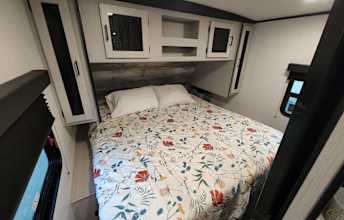 Cozy RV rental bedroom: A full bed with floral bedding, overhead cabinets, and side windows create a comfortable travel stay.. Heartland Mallard 2022