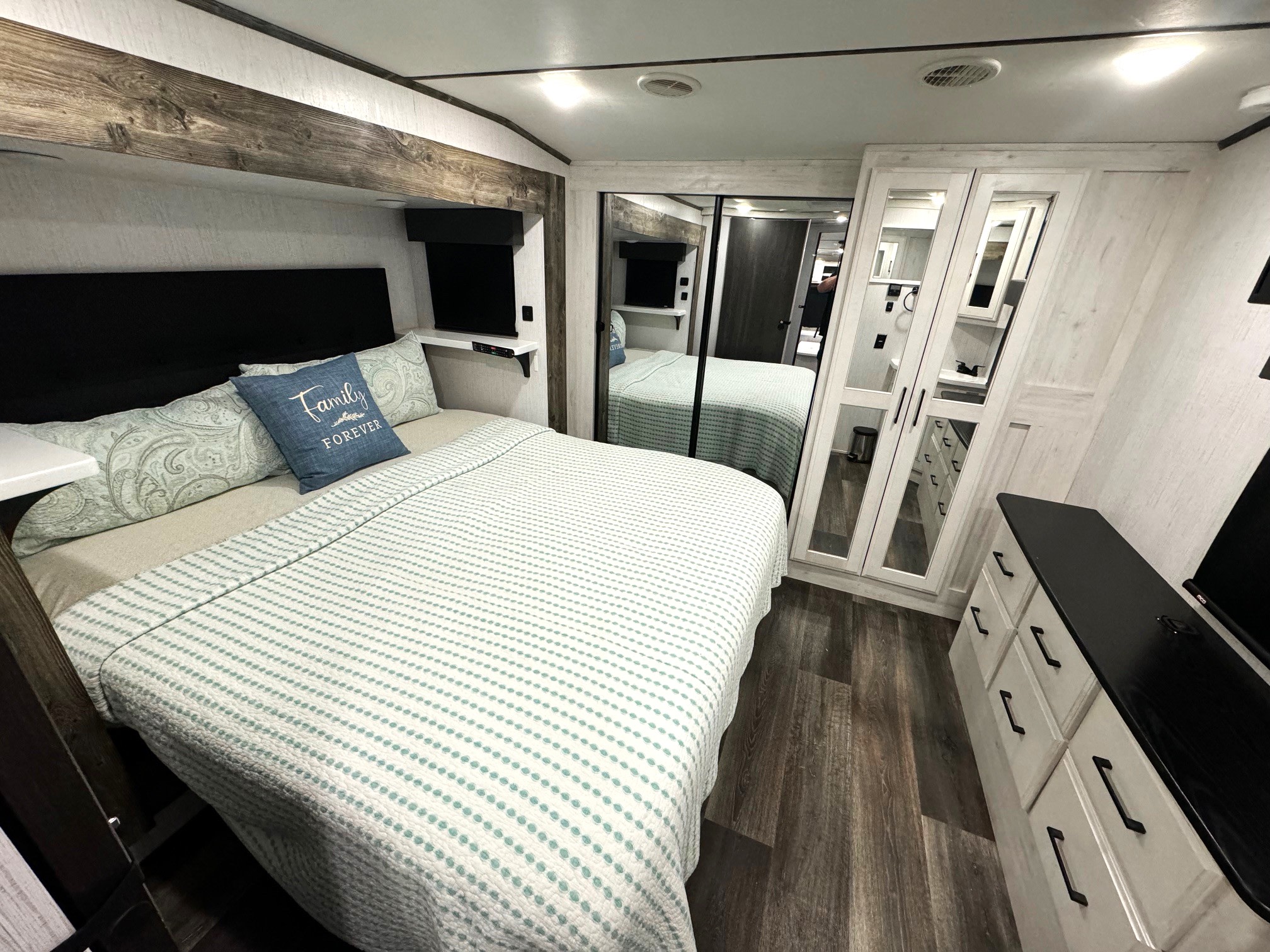 Modern RV rental bedroom featuring a comfortable bed, mirrored closet, dresser, and built-in TV.. Heartland Bighorn 2022