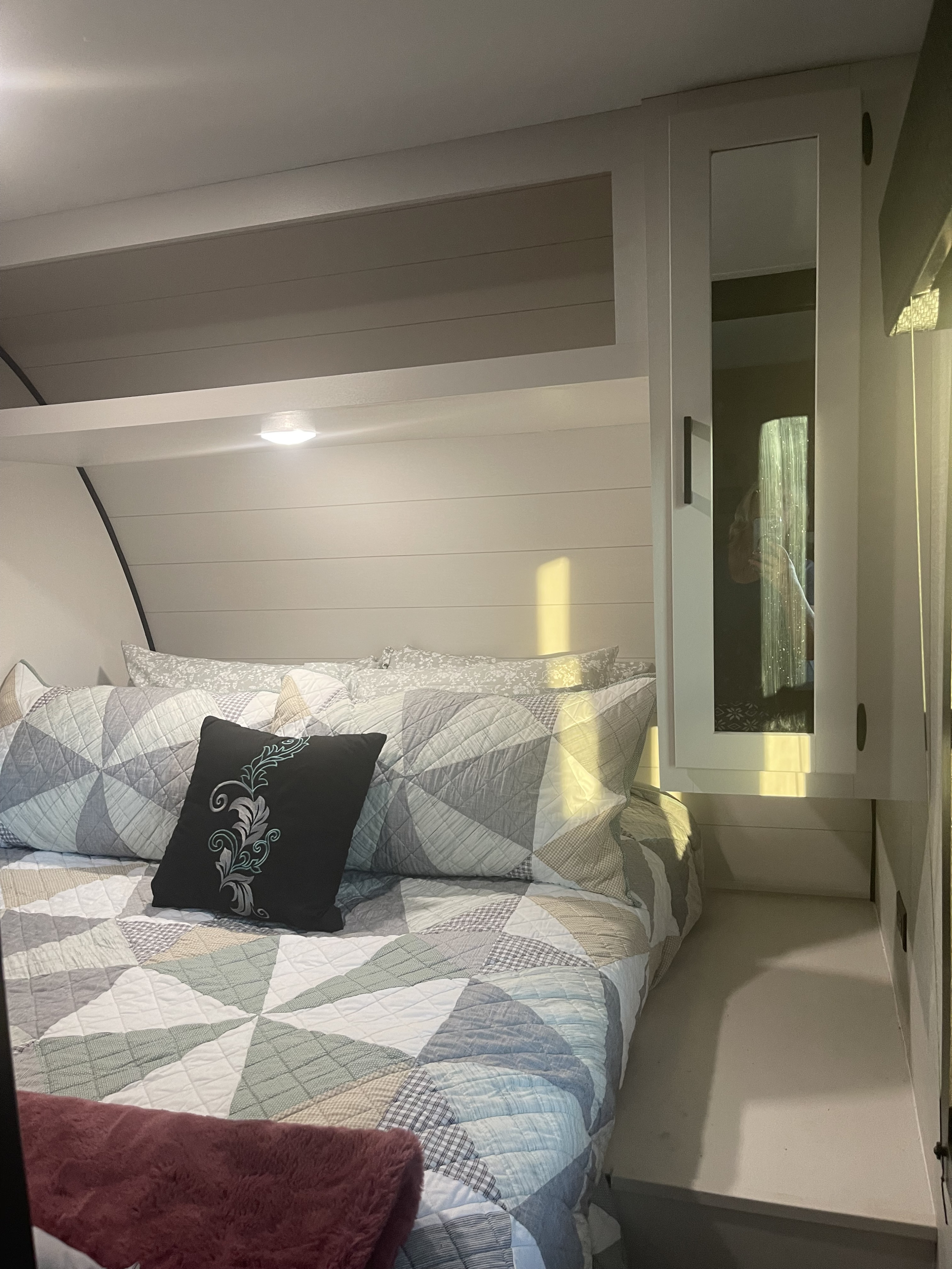 Cozy RV rental bedroom features a geometric quilt, decorative pillows, shiplap walls, and a mirrored cabinet, perfect for travel comfort.. Starcraft Autumn Ridge 2024