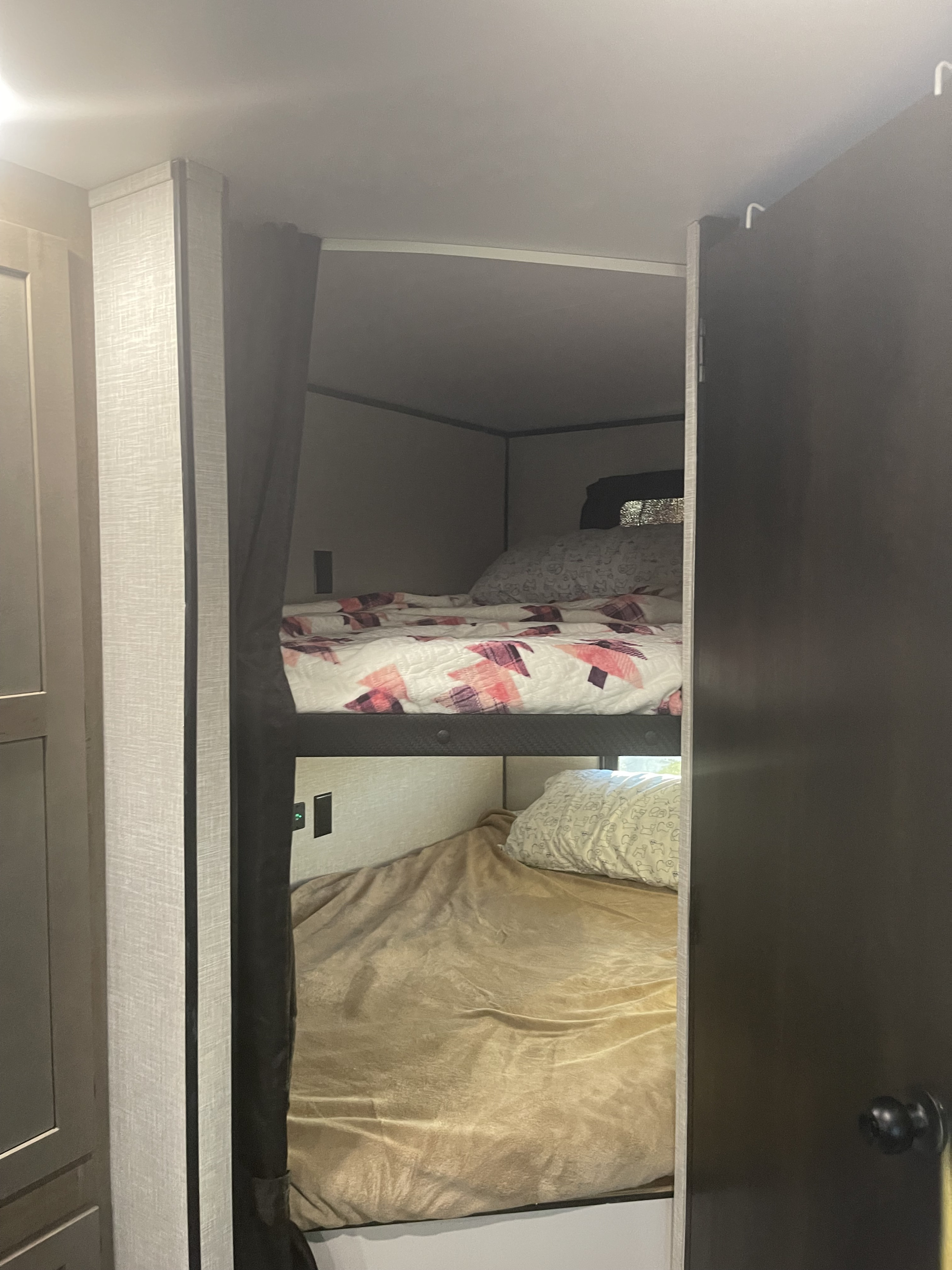 Inside an RV rental, two bunk beds with patterned quilts and pillows offer a compact, comfortable sleeping space.. Starcraft Autumn Ridge 2024