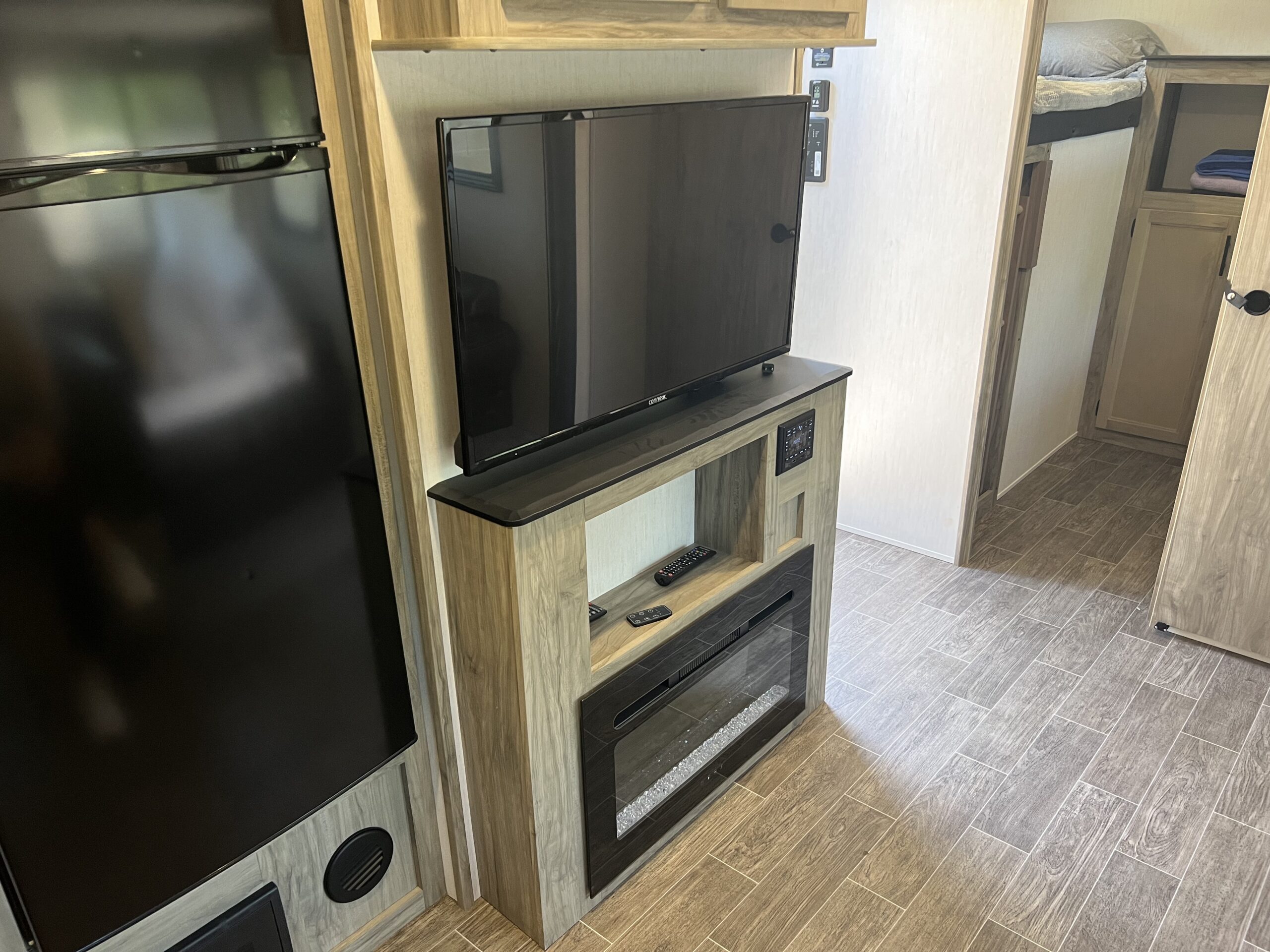 This RV rental features a sleek entertainment center with a TV, fireplace, and refrigerator, plus a peek at bunk beds.. Forest River Alpha Wolf 2022