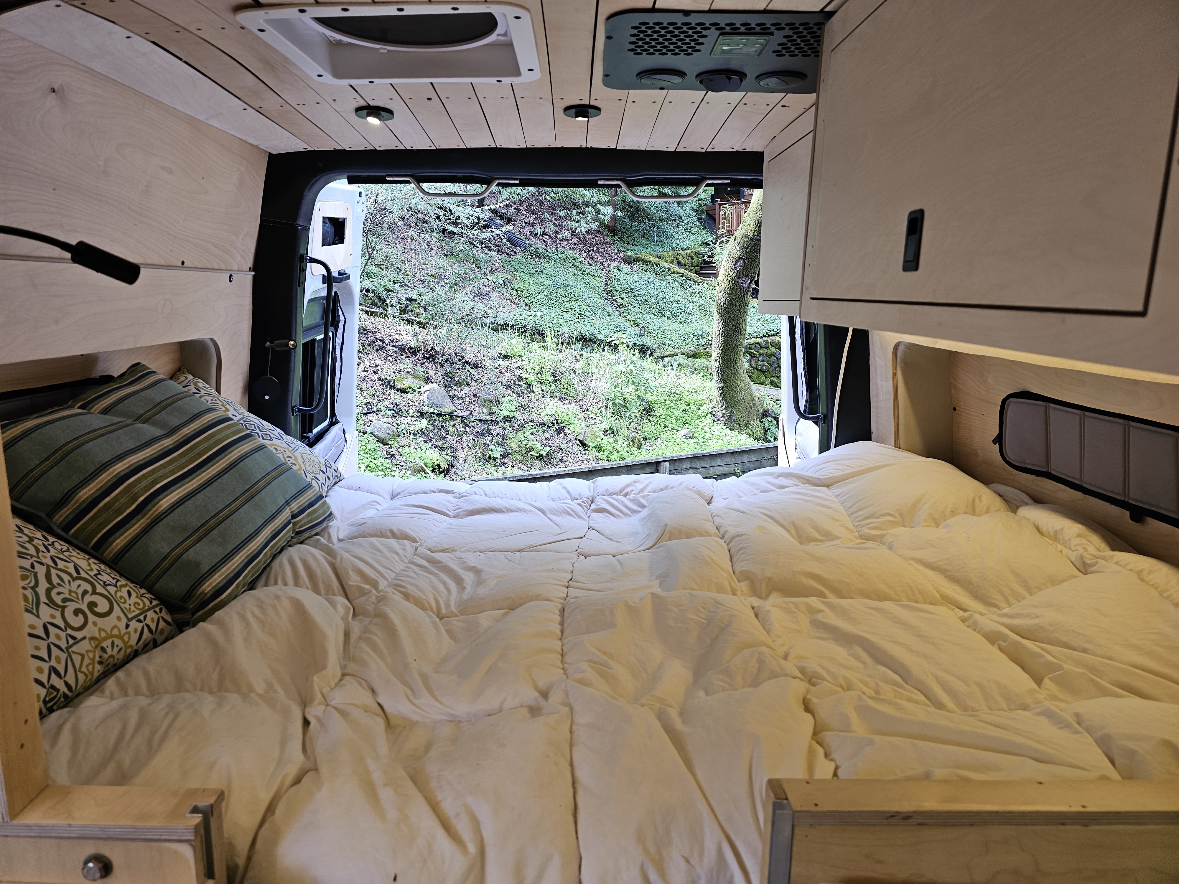 Relax in this cozy RV rental! Enjoy the comfy bed and stunning view of a lush green forest through the open back doors.. mercedes 144 High Roof AWD 2024