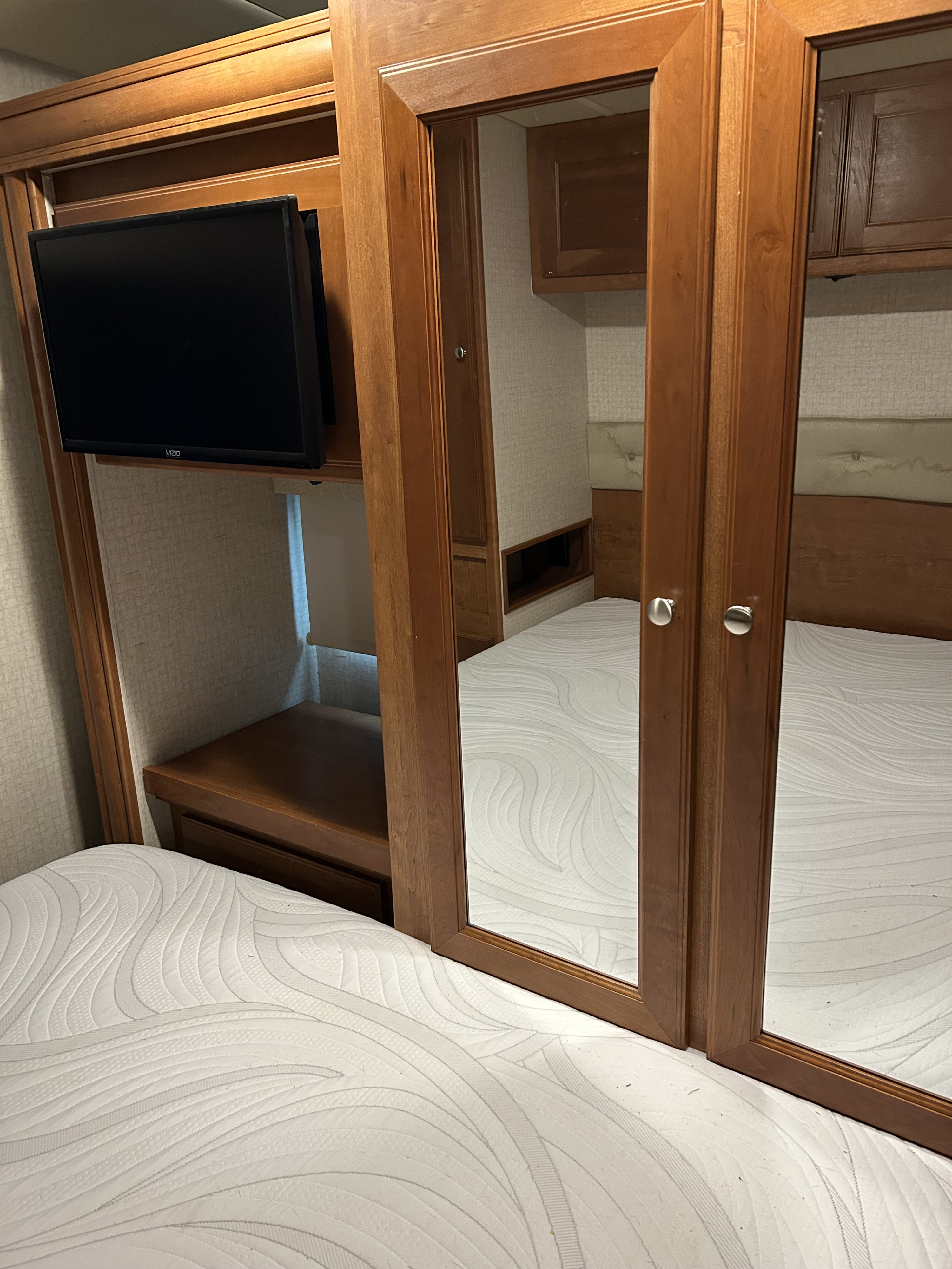 Cozy RV rental bedroom with patterned white mattress, wall-mounted TV, and mirrored wooden cabinets.. Winnebago Sunstar 2017