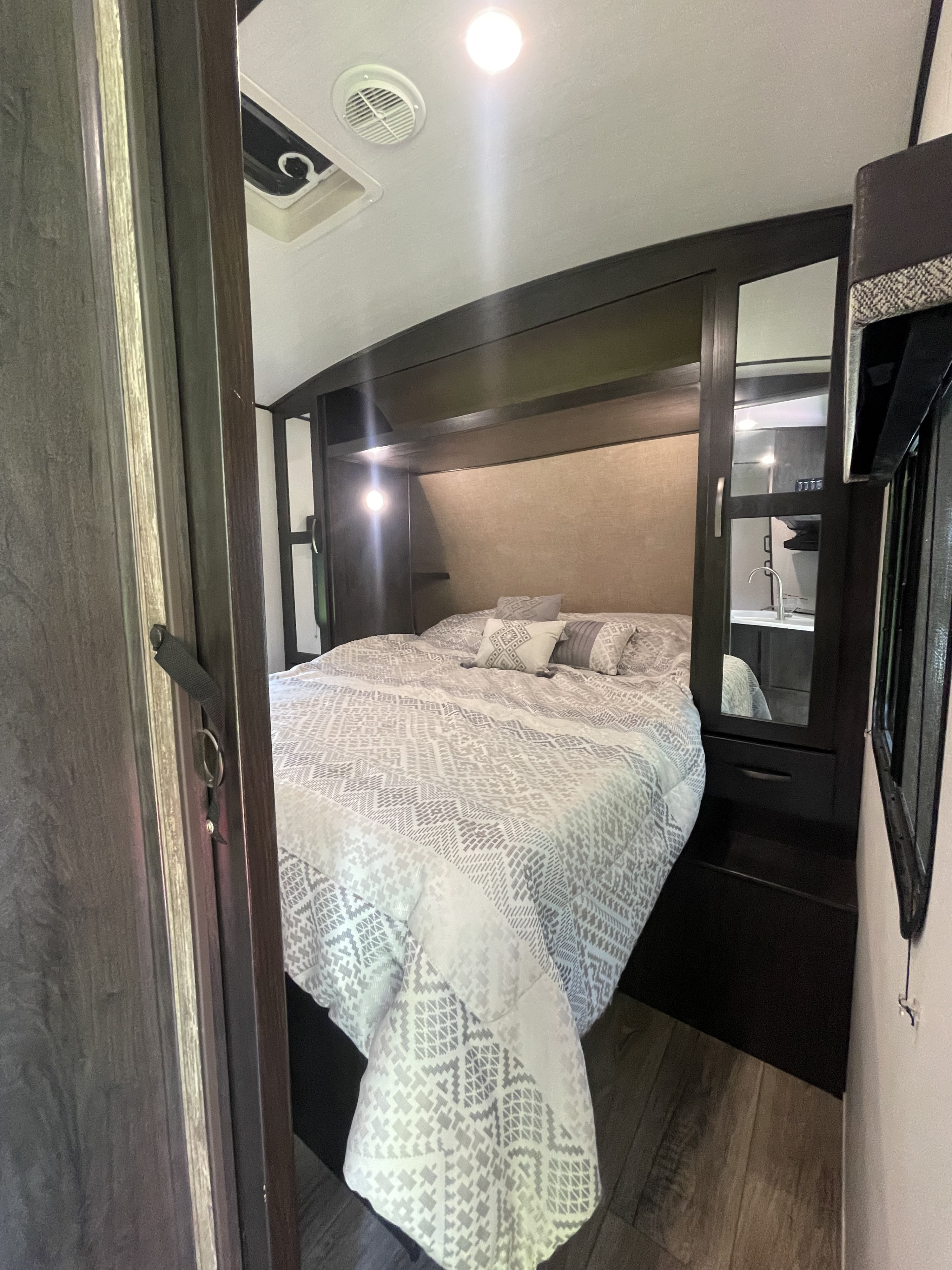 Inviting RV rental bedroom features a patterned queen bed, dark wood built-ins, mirror, and ceiling lights.. Forest River Surveyor Legend 2019
