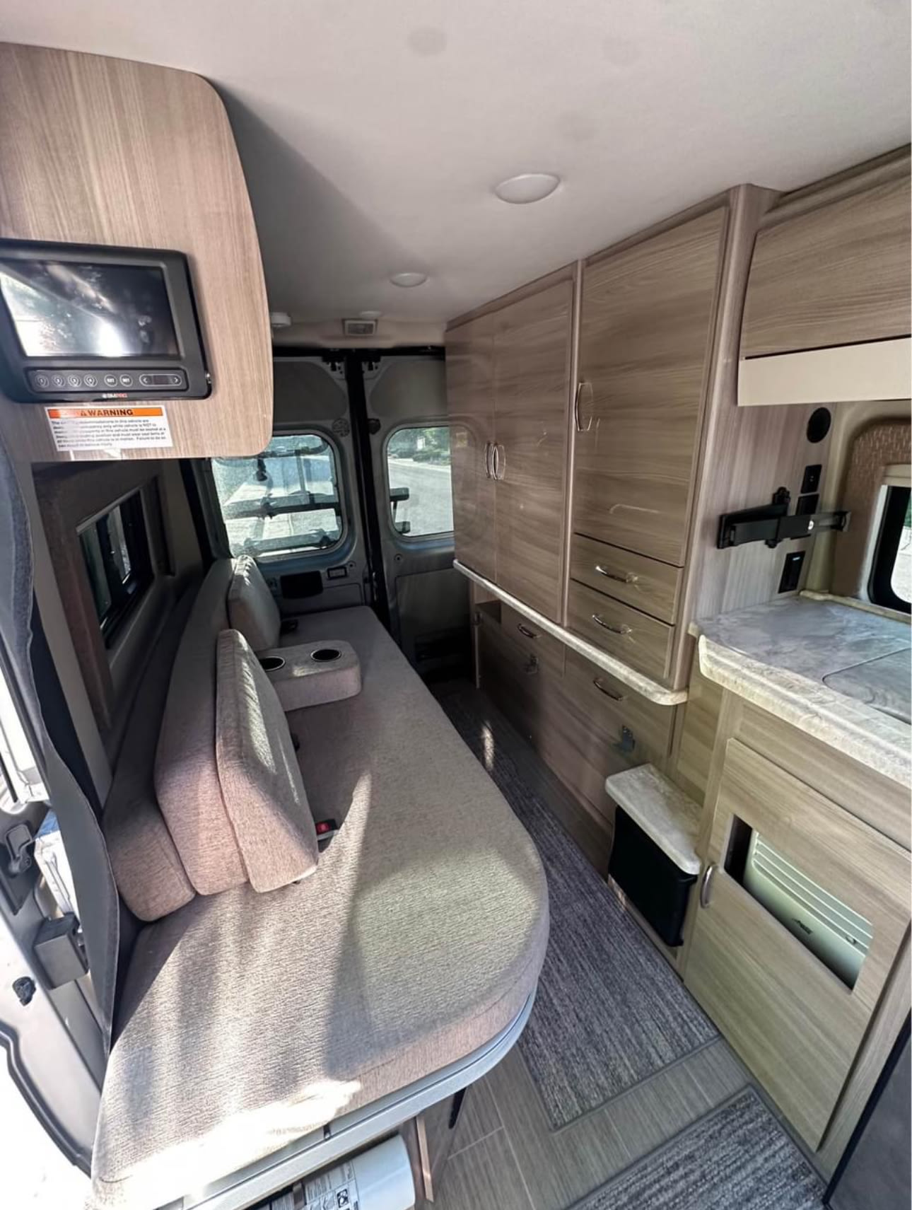 RV rental interior: cozy couch/bed, wood cabinets, and a compact kitchen. Ready for your next adventure!. Thor Motor Coach 18T 2022