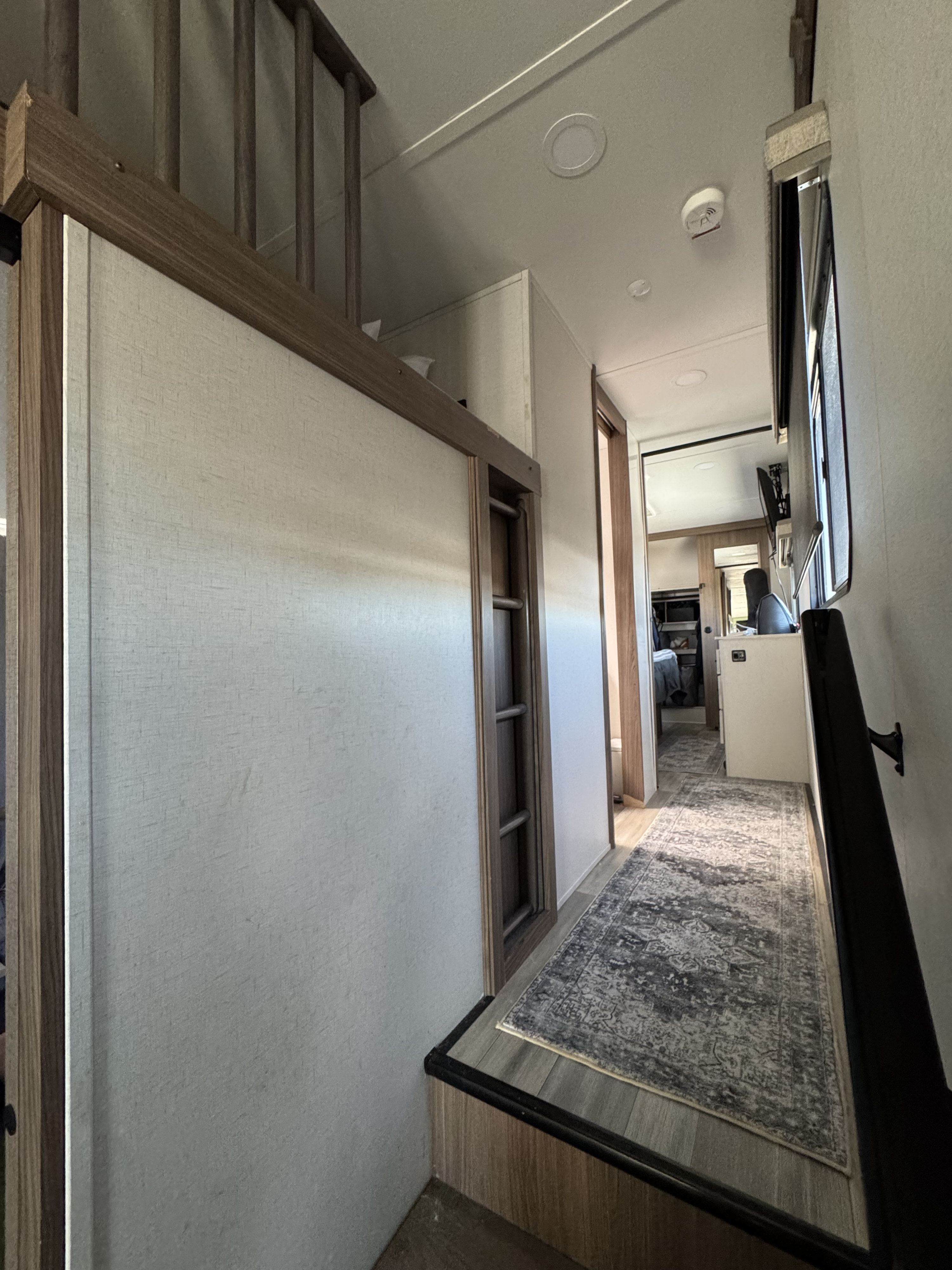 RV rental interior showcasing a modern hallway with light walls, wood trim, step-down, and a cozy rug.. Alliance Paradigm 2023
