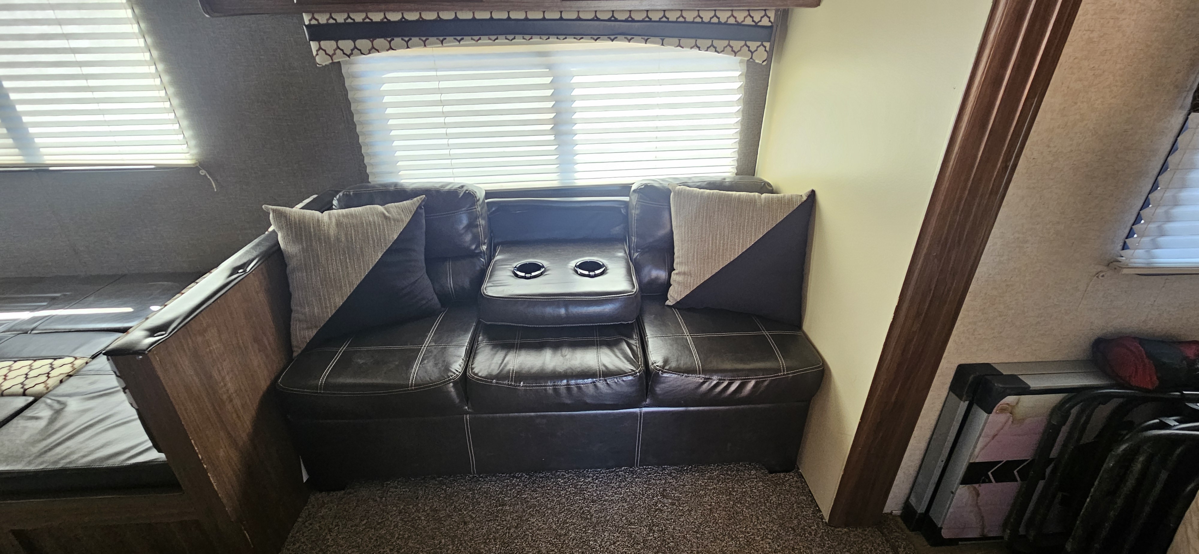 Relax in this RV rental's cozy interior, featuring a dark leather sofa with cup holders, pillows, and window blinds.. Heartland RVs Prowler Lynx 2018
