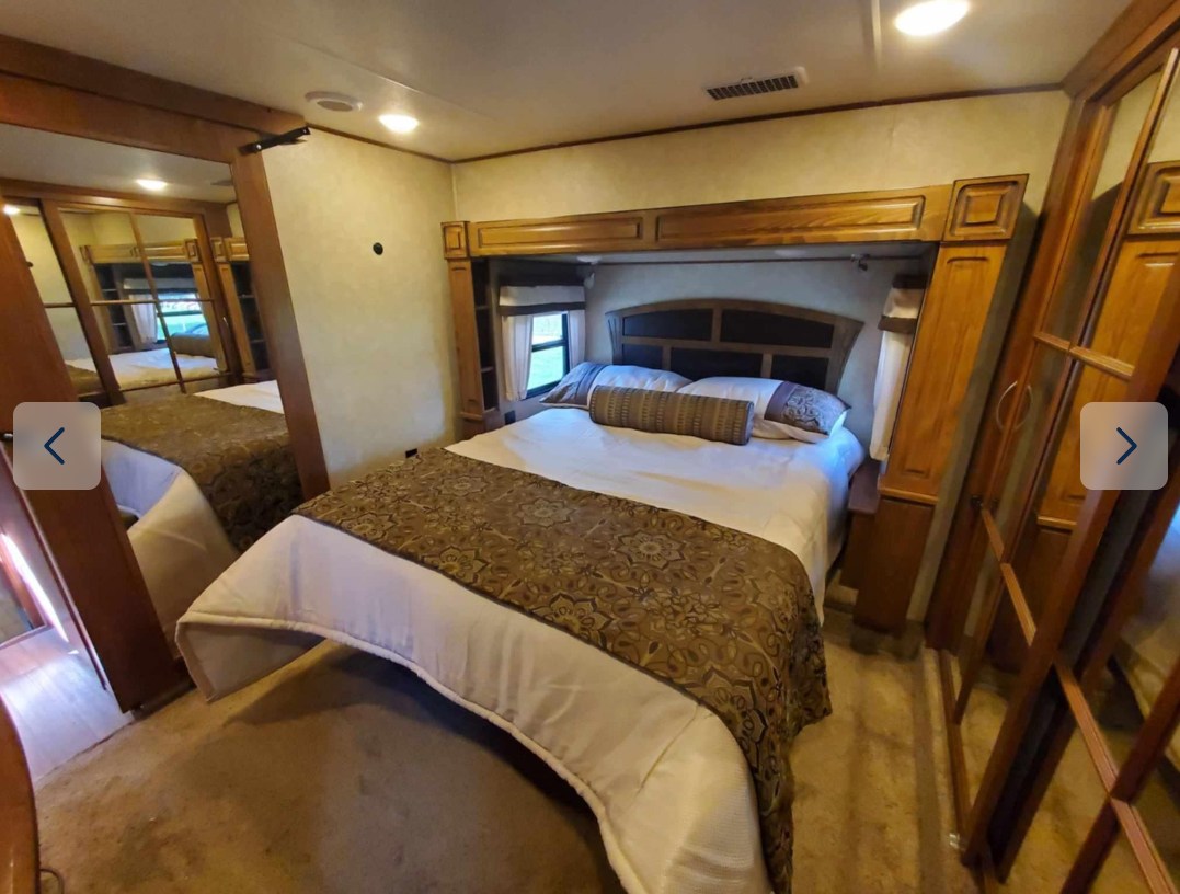 Spacious RV rental bedroom featuring a large bed, built-in wooden cabinetry, and mirror. Comfortable interior.. Forest River Palomino Compass 2016