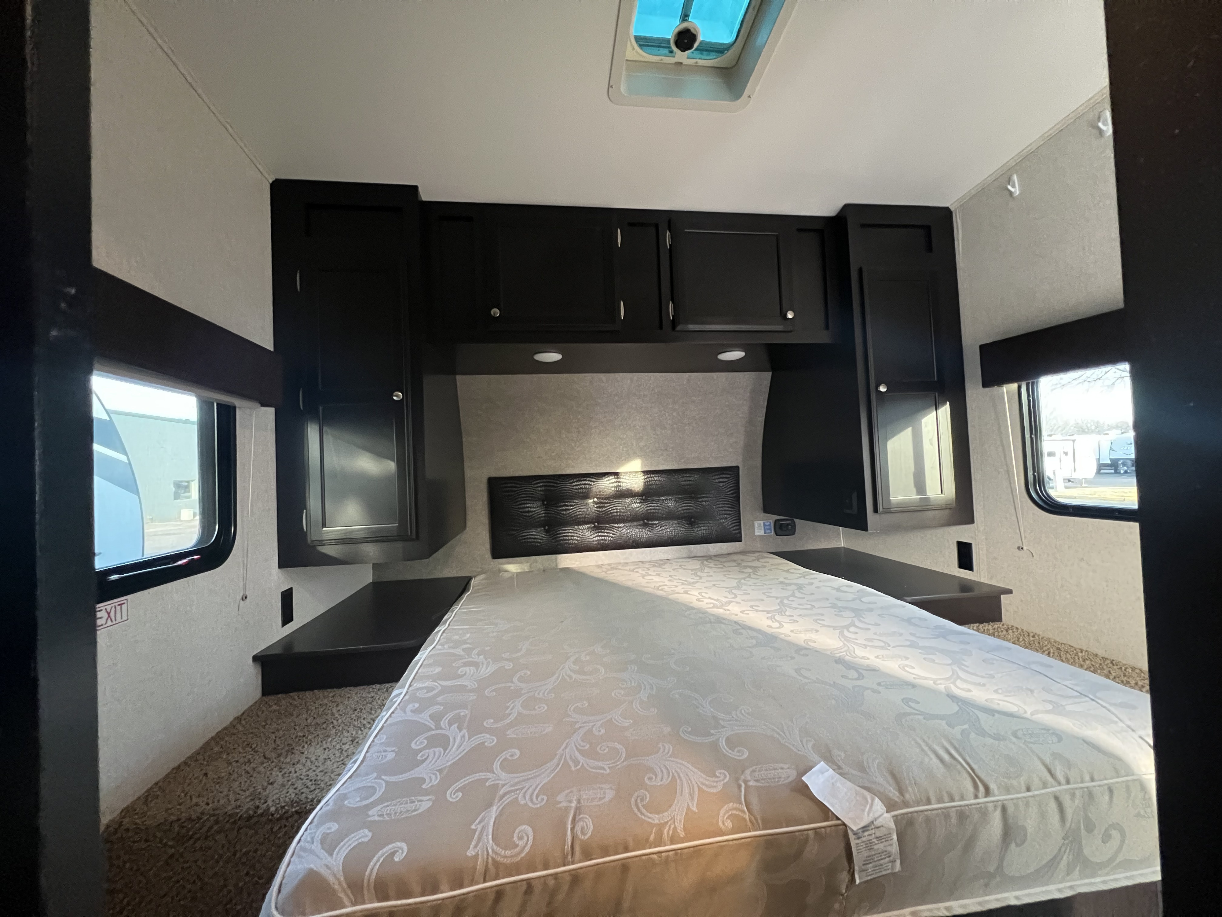 RV rental bedroom featuring a large bed with patterned mattress, dark cabinetry, and dual windows, offering comfort and light.. Jayco Octane 2018