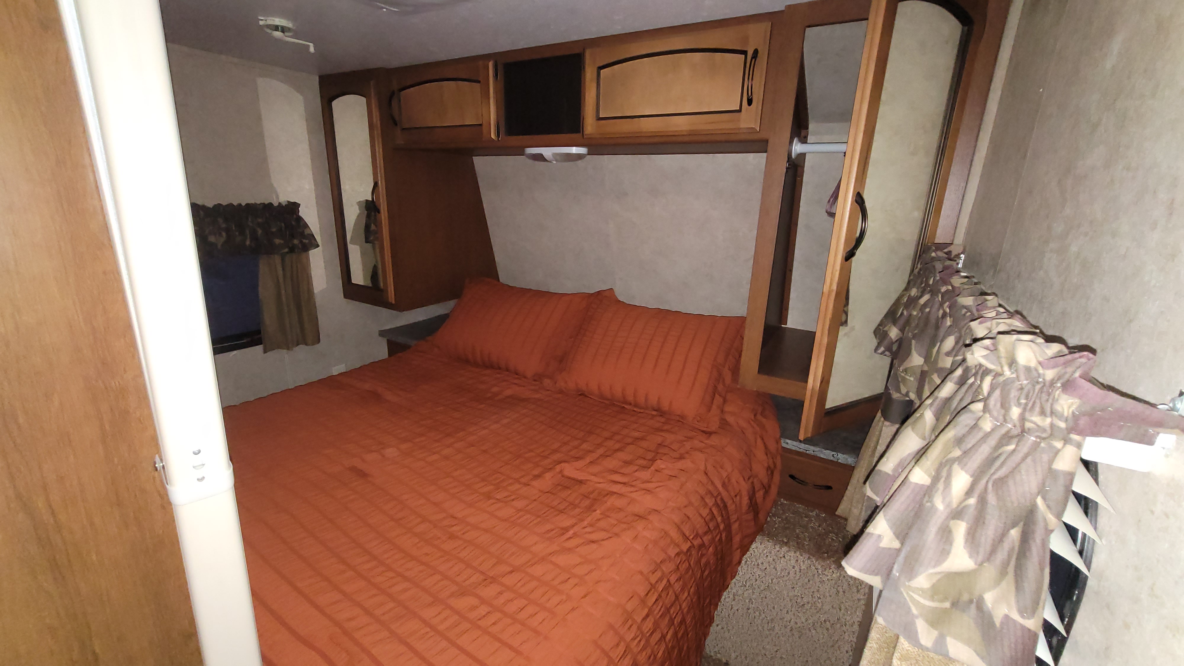 Comfortable RV rental bedroom with orange bed, overhead cabinets, and closet space, perfect for your travel adventure.. Keystone RV Springdale 2012