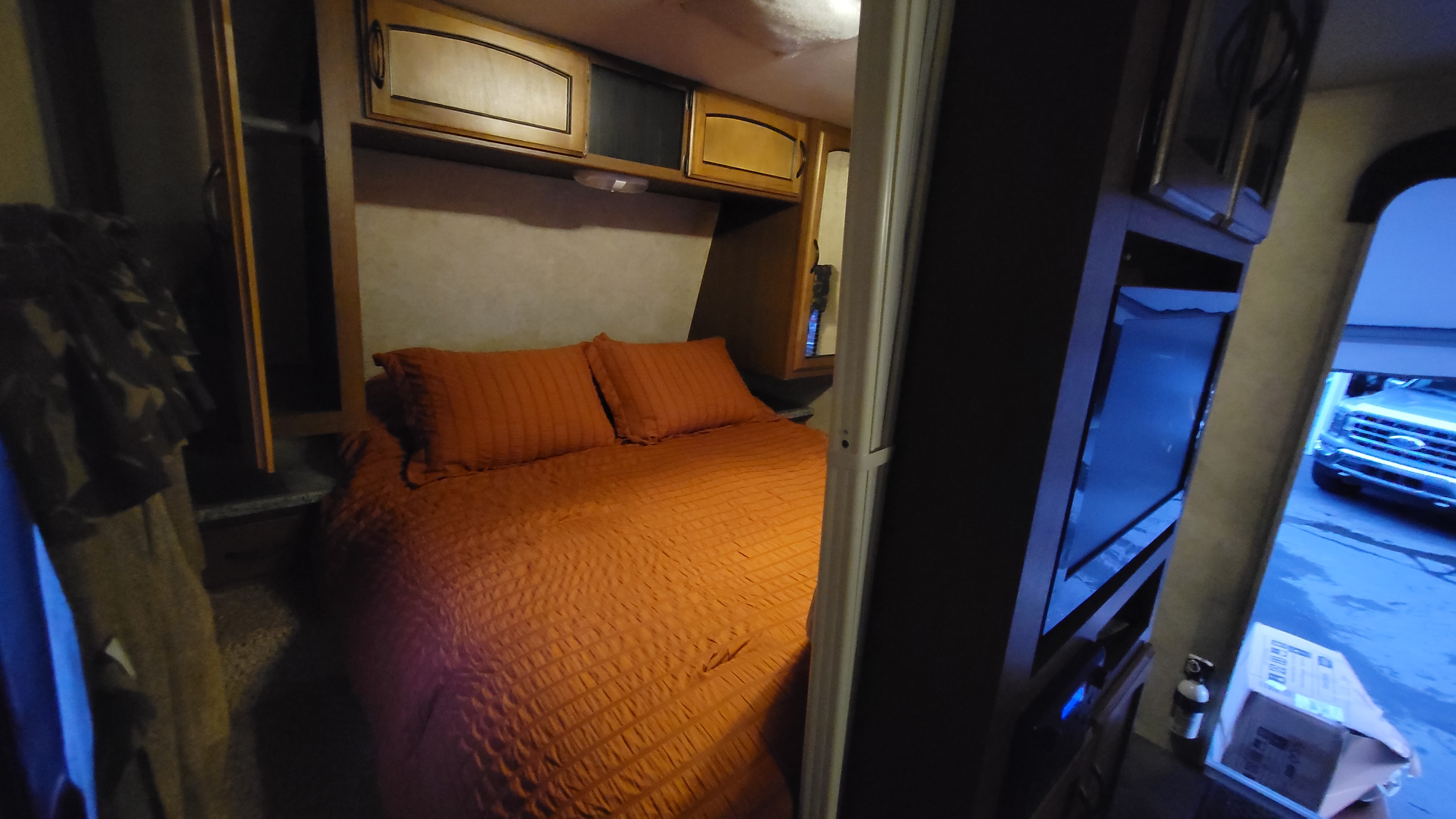 Cozy RV rental bedroom: orange bed, overhead cabinets, and exterior vehicle view, ideal for travel comfort.. Keystone RV Springdale 2012