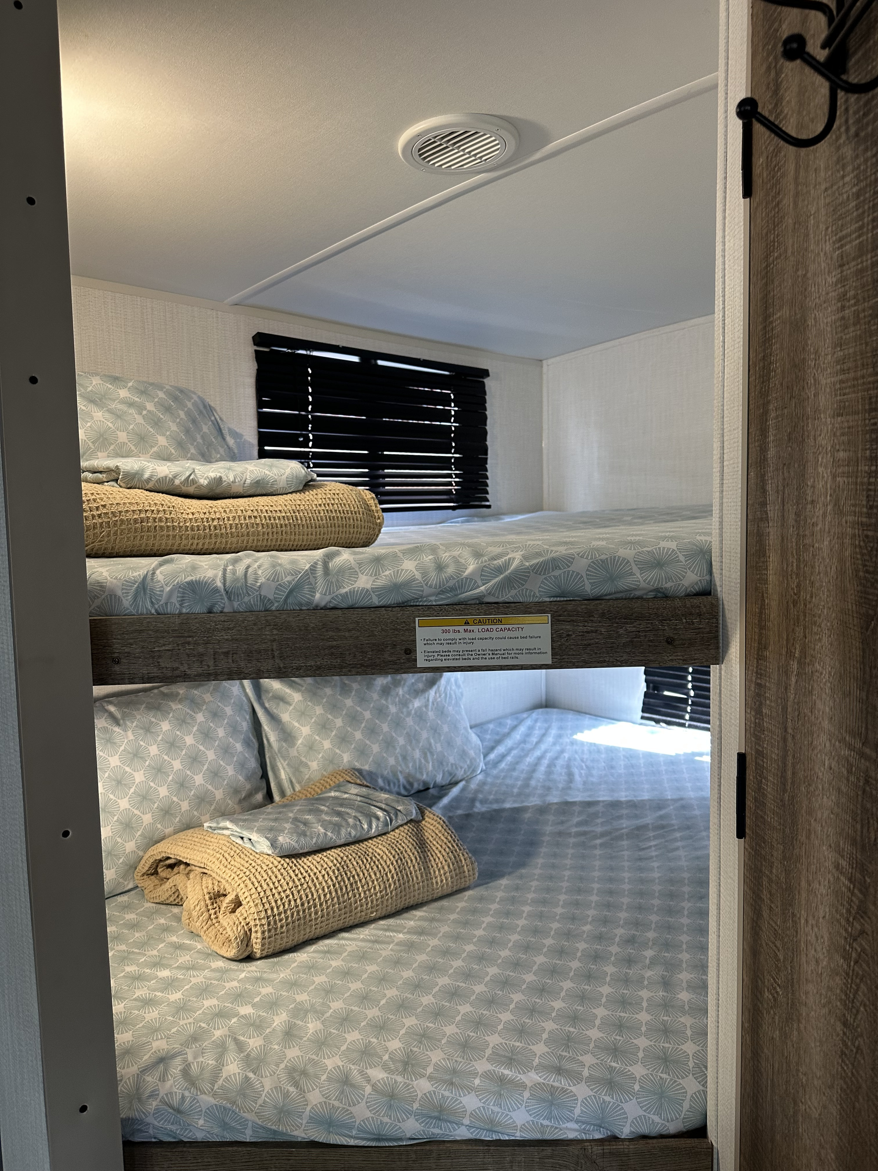Light blue patterned sheets on cozy RV rental bunk beds. The top bunk has a 300 lbs max load capacity warning label.. Heartland RVs Eddie Bauer Rear bunkhouse with front bedroom 2024