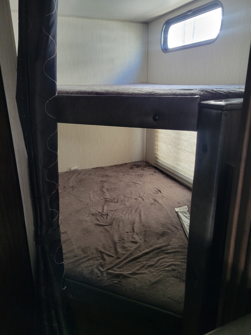Cozy RV rental interior featuring two bunk beds with dark blankets and a window, ideal for extra sleeping space.. Forest River Patriot 2021