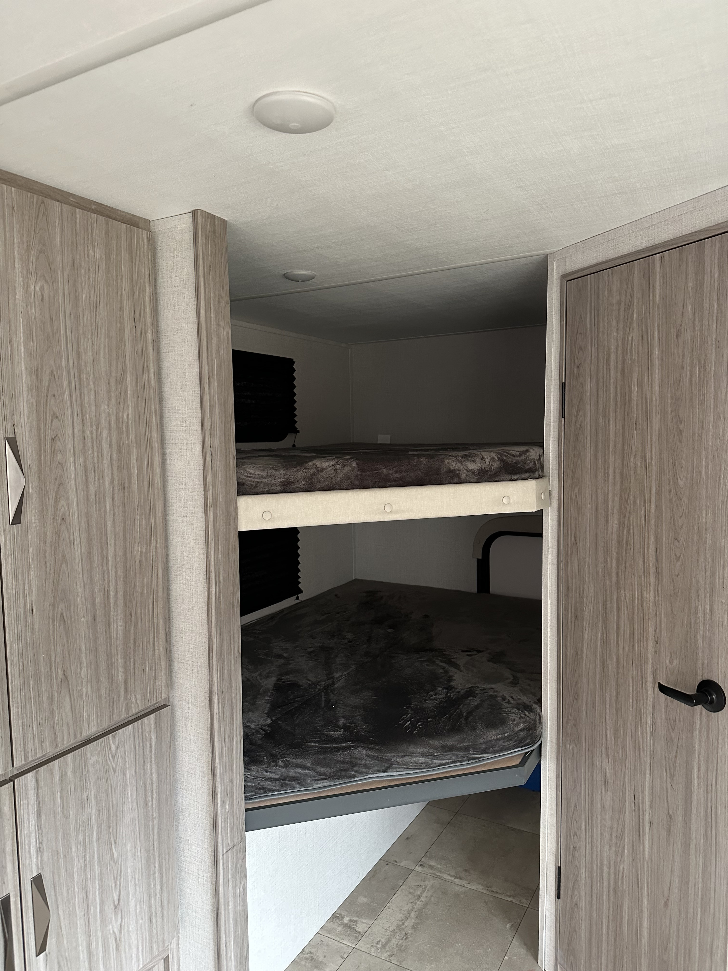 View of the bunk bed area in an RV rental, featuring two beds with dark blankets, light wood cabinets, and a door.. Keystone RV Passport SL Ultra Lite 2024