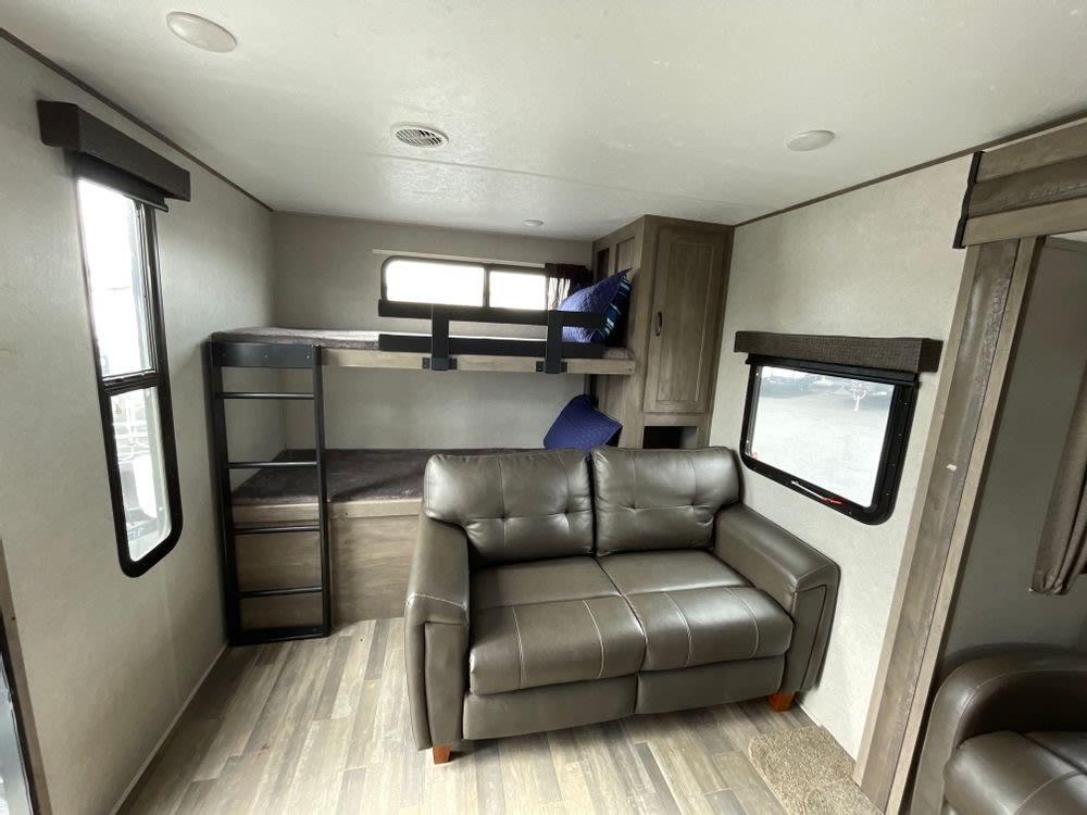 Spacious RV rental interior featuring comfortable bunk beds, plush couch seating, and windows, ideal for family travel.. Forest River Vibe 2021