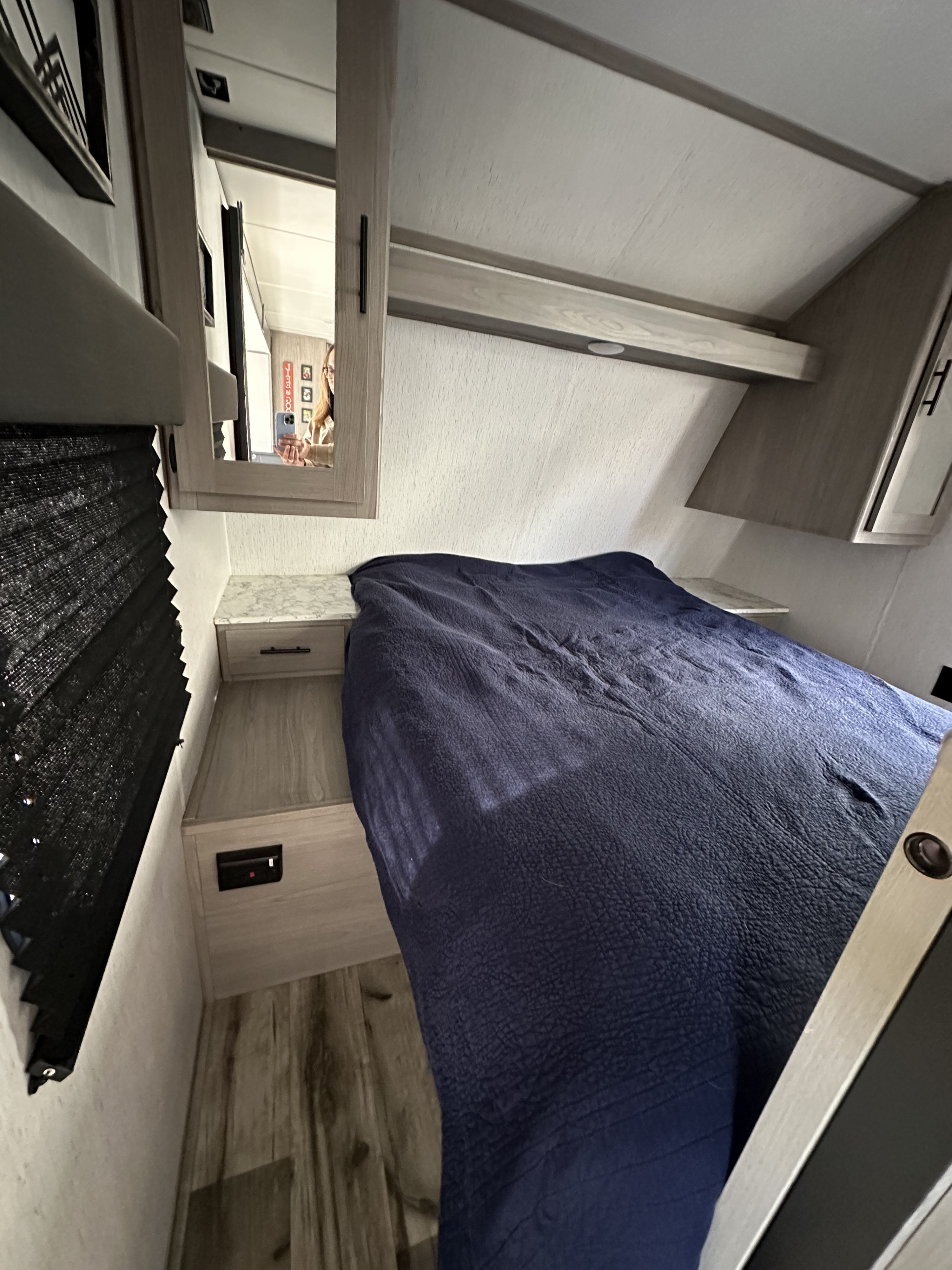 Cozy RV rental bedroom showing a dark blue bed, nightstand, and mirror reflecting the person taking the photo.. Dutchmen Coleman Lantern 2022