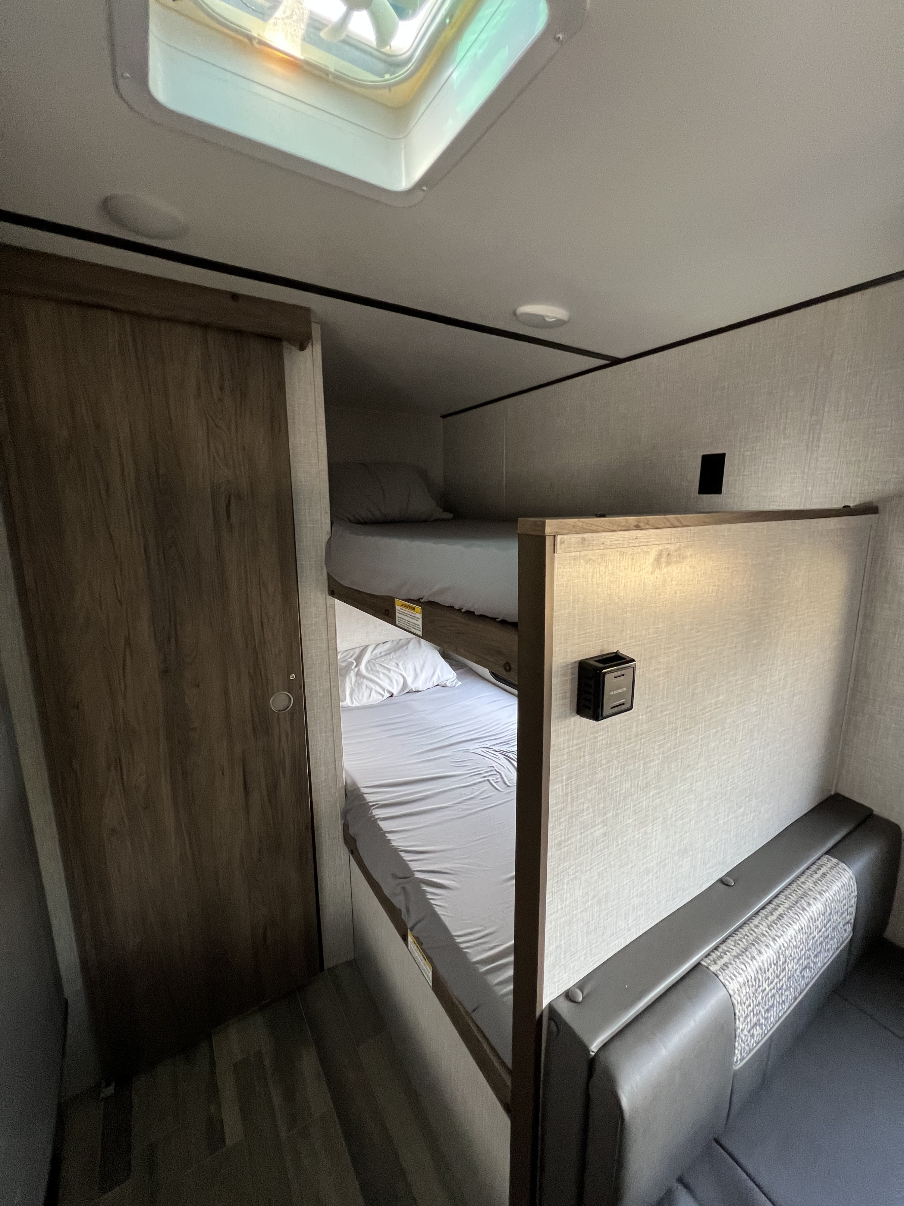 Cozy RV rental interior: bunk beds with light bedding, a sliding door, and skylight above. Perfect sleeping area.. Crossroads RV Zinger Lite 2021
