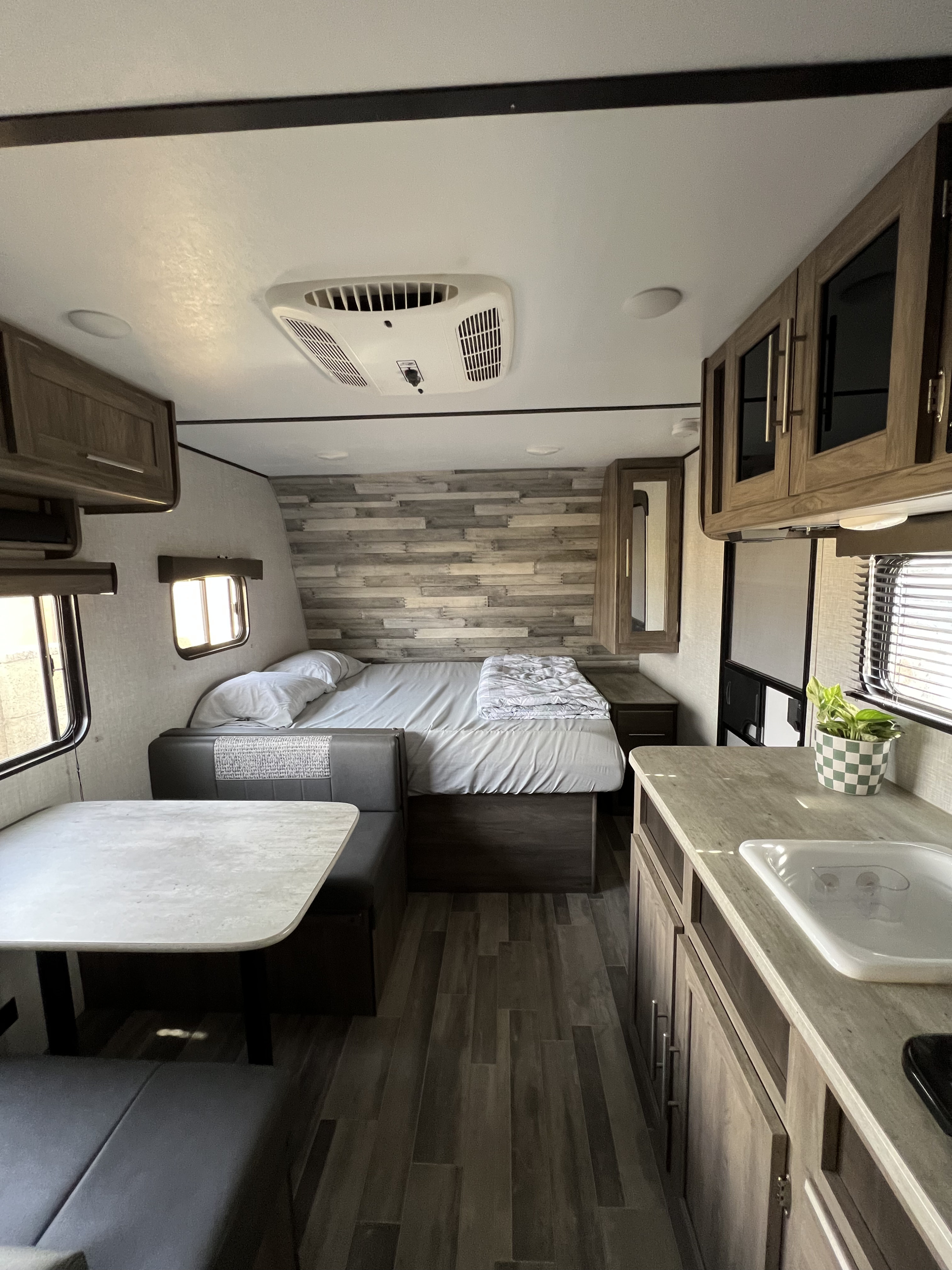 Inside a cozy rv rental, featuring a comfortable bed, dinette, and compact kitchen area with light wood accents.. Crossroads RV Zinger Lite 2021