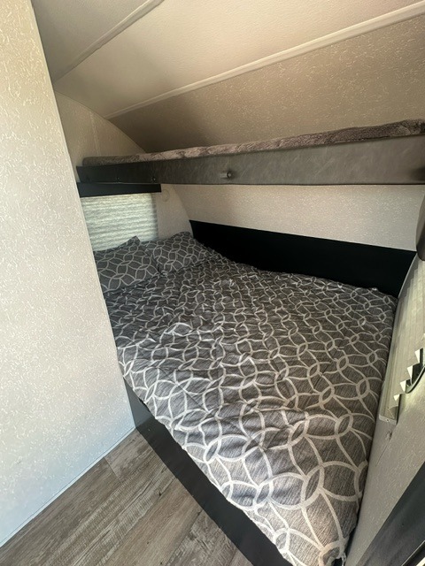 RV rental bedroom with a gray patterned lower bed and an upper bunk. Perfect for family adventures!. Forest River Wolf Pup 2021
