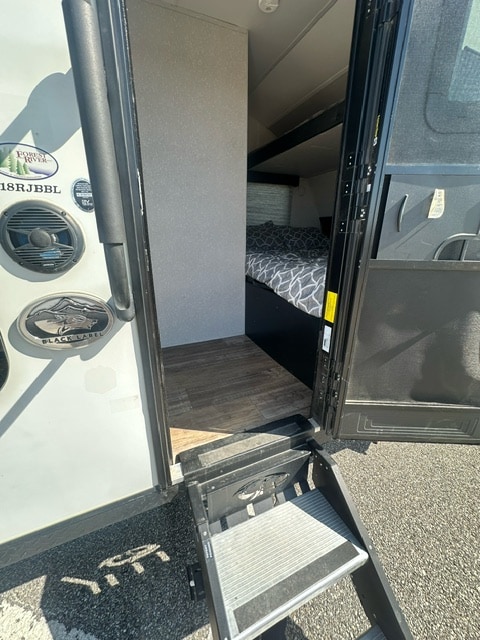 Steps lead into this RV rental, showcasing its open door and a cozy bedroom inside with patterned bedding.. Forest River Wolf Pup 2021