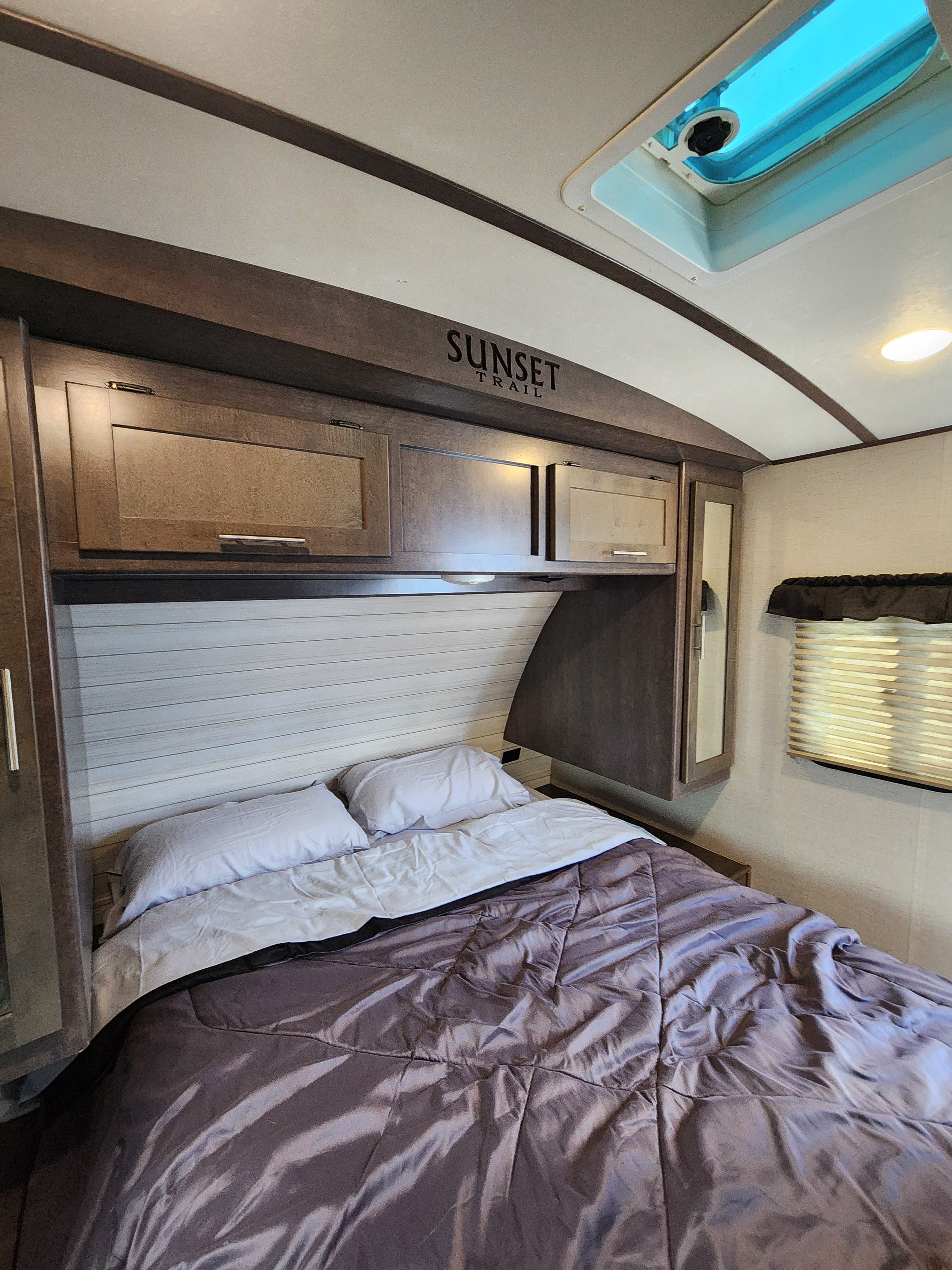 Inside an RV rental: a cozy bedroom featuring overhead cabinets, a window, and a bed with a ceiling skylight.. Crossroads Sunset Trail Super Lite 2018
