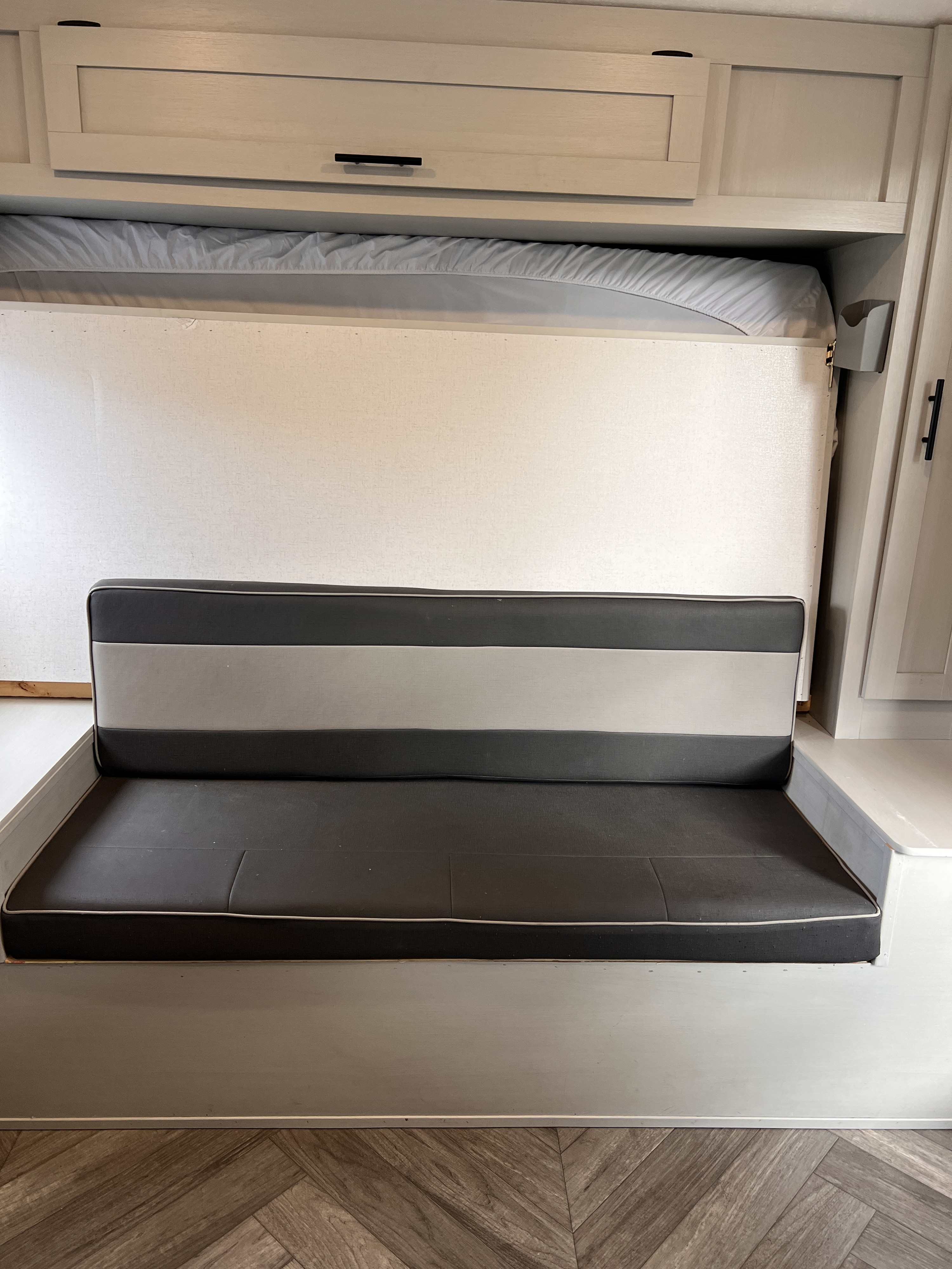 RV rental interior showing a sofa with gray/black cushions, a fold-down bed above, and overhead cabinets.. Forest River Salem FSX 2021