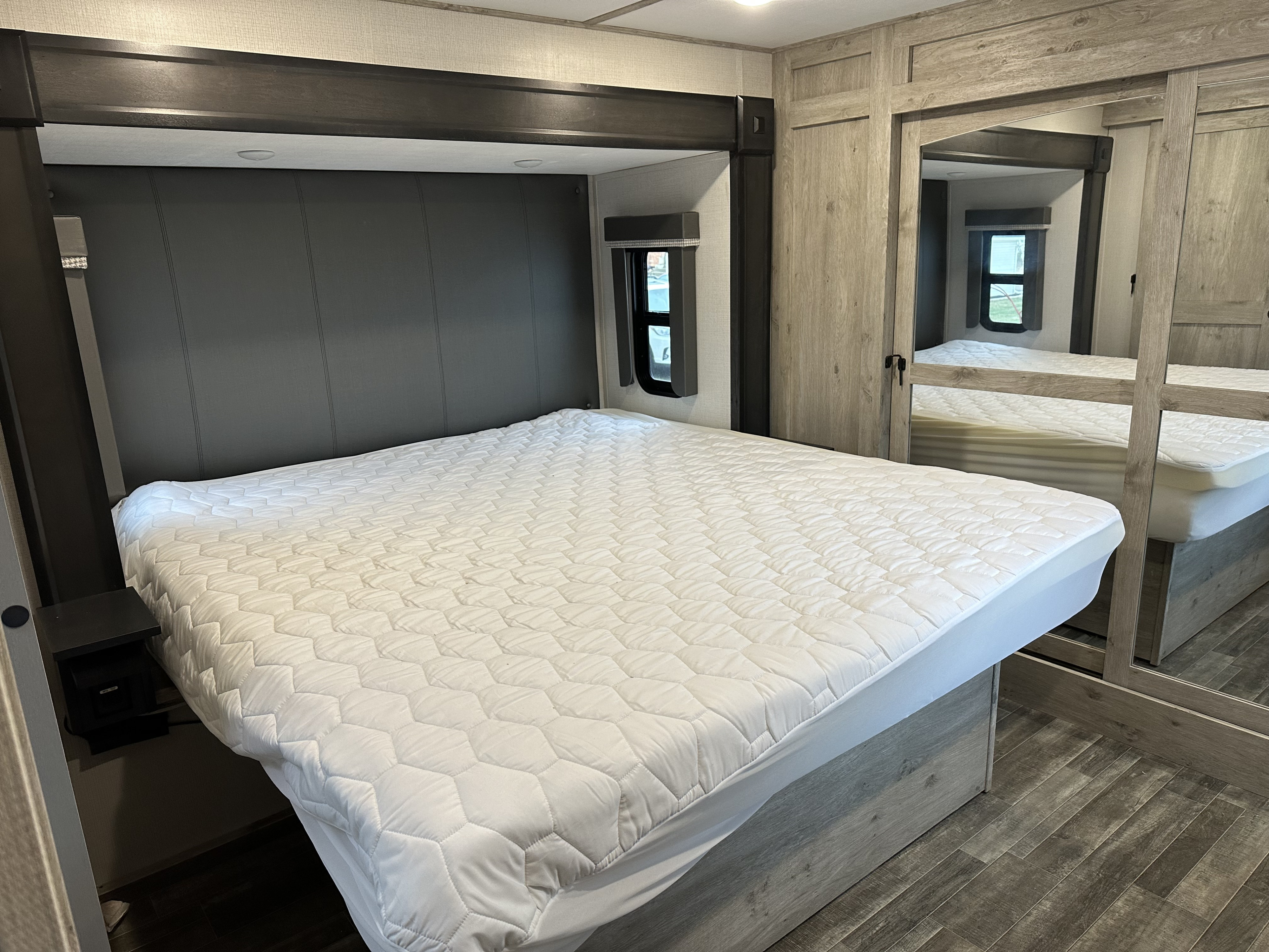 Comfortable RV rental bedroom featuring a large bed with a quilted mattress pad, window, nightstand, and mirrored closet.. Keystone RV Avalanche 2023