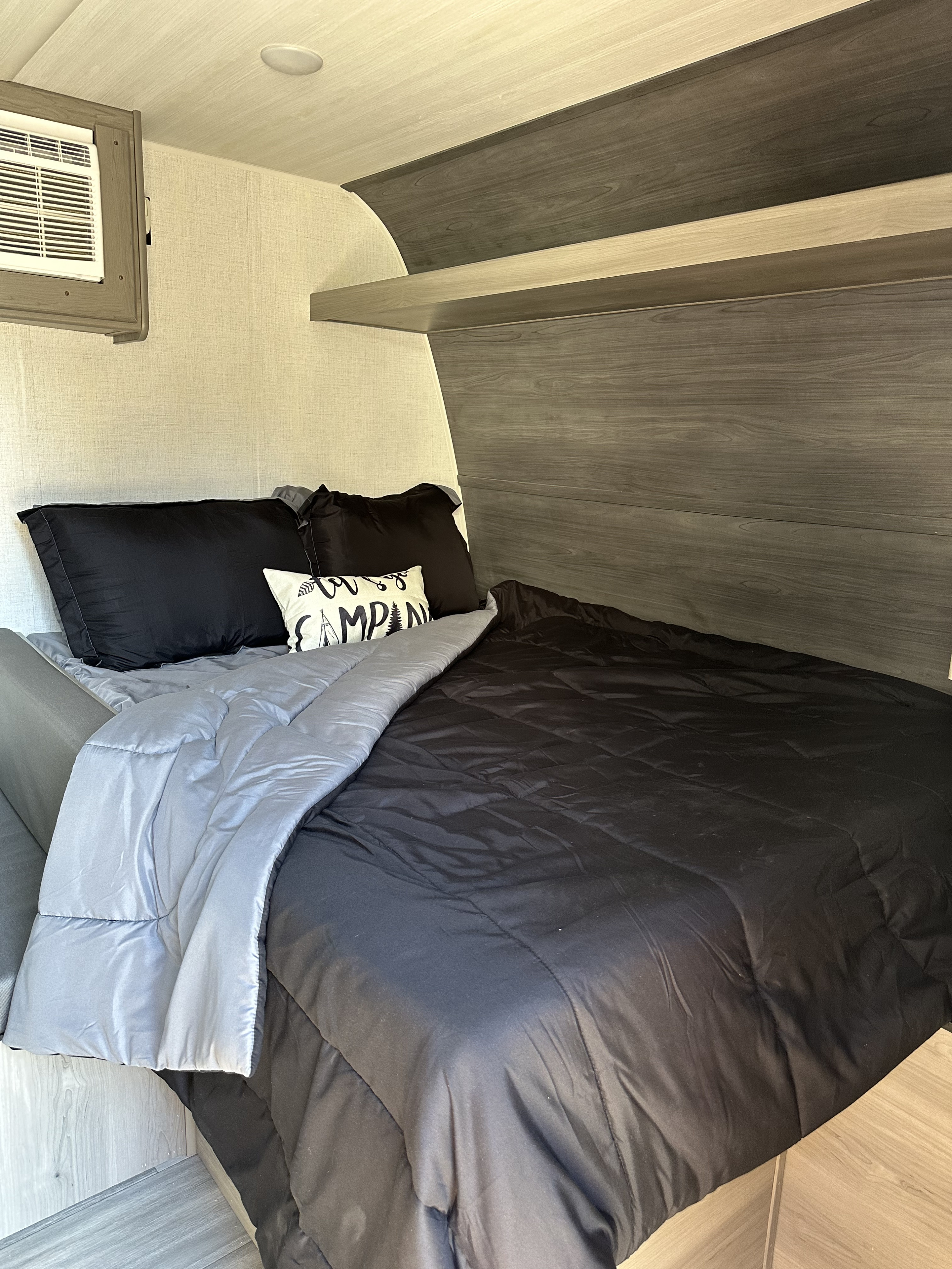 Inside this RV rental, find a comfortable bed with black and grey bedding, a decorative pillow, overhead shelves, and AC.. Keystone RV Hideout Sport 2024