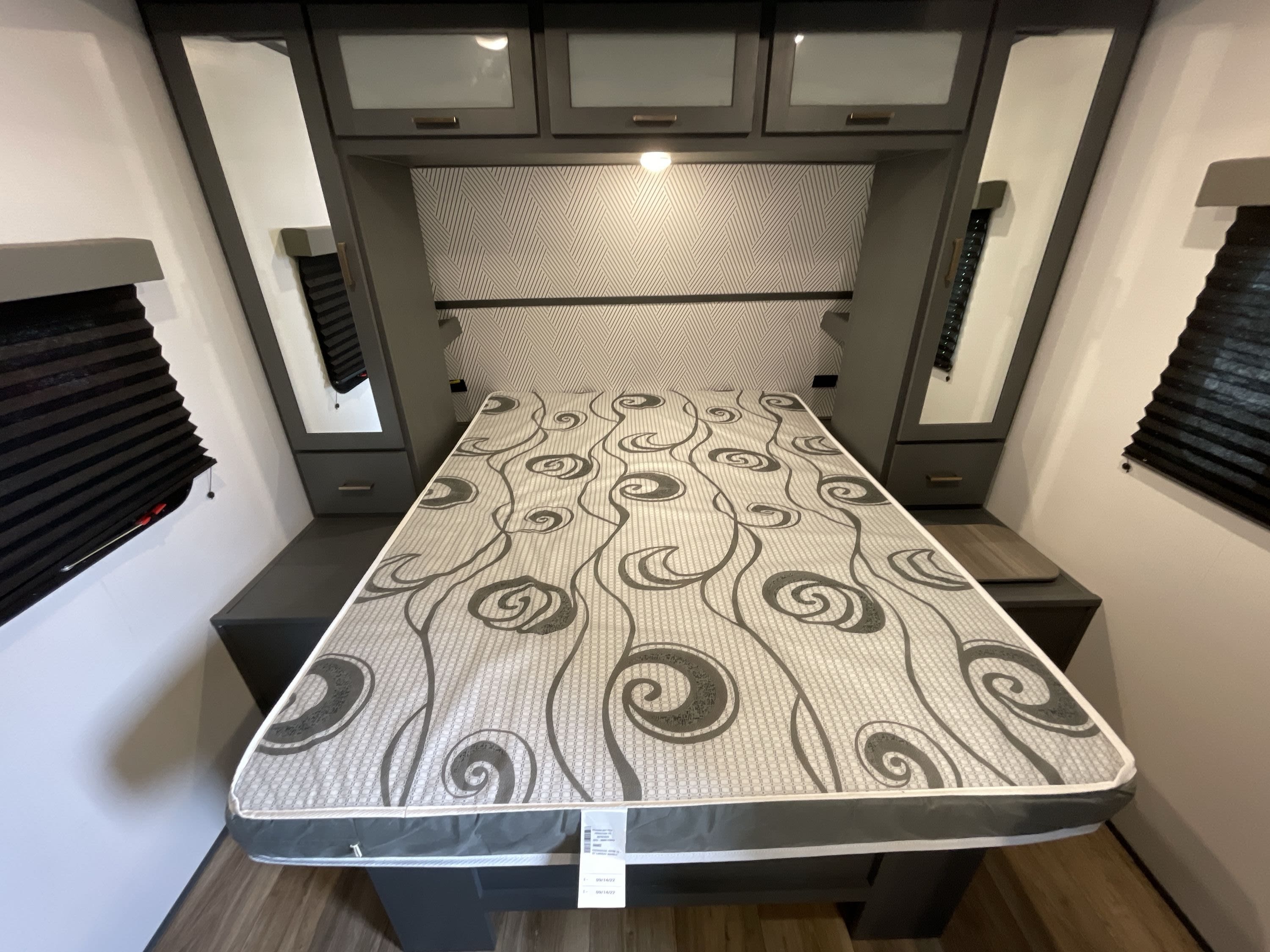 Compact RV rental bedroom with patterned mattress, dark cabinetry, and wall-mounted blinds, offering a cozy sleeping space.. Keystone Bullet 2023