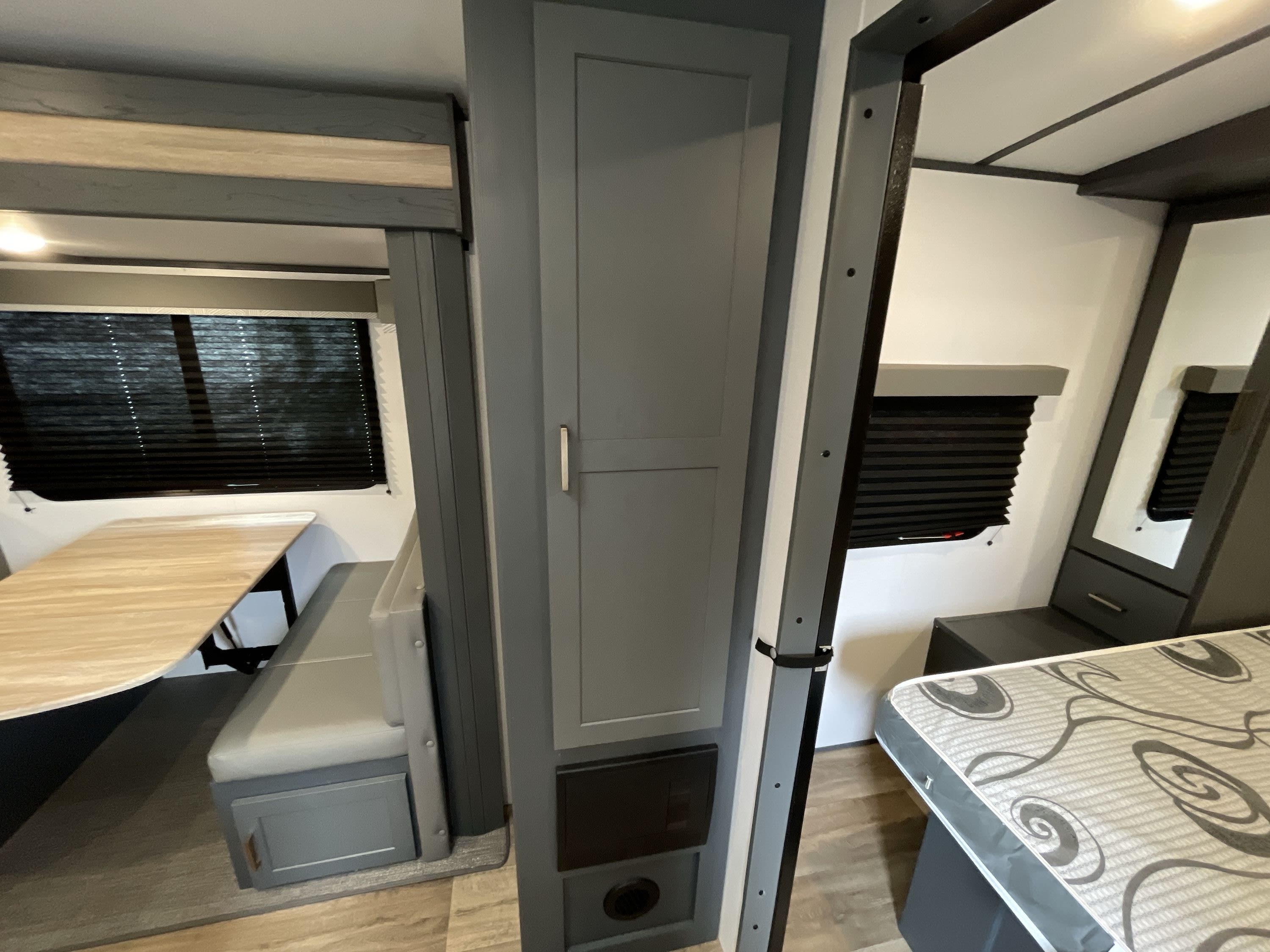 RV rental interior showcasing a compact dining area with bench, central cabinet, and part of the bedroom with a patterned mattress.. Keystone Bullet 2023