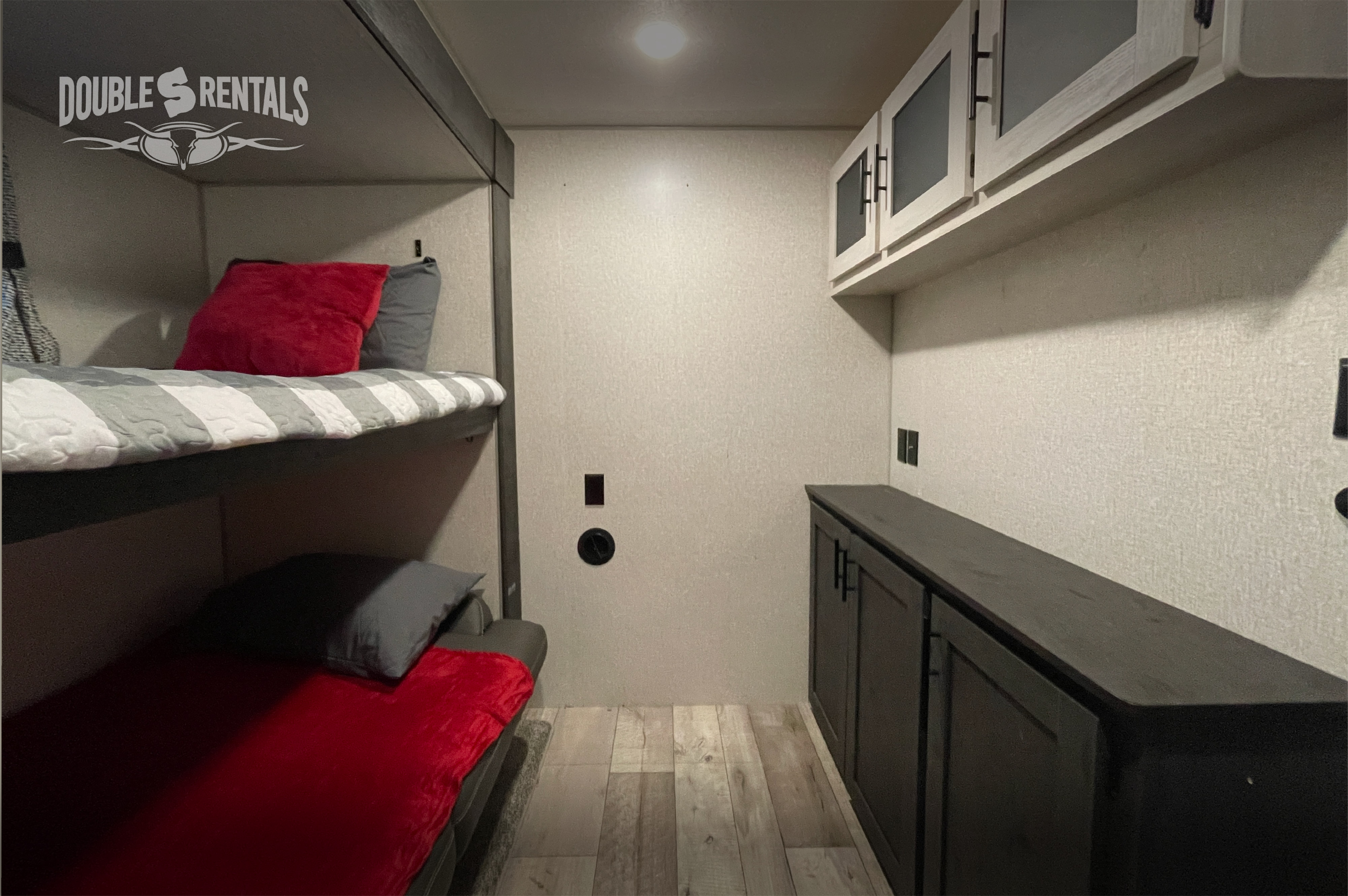 RV rental interior: bunk beds with red and grey bedding, light upper cabinets, and dark lower storage.. K-Z Manufacturing Sportsmen 2022