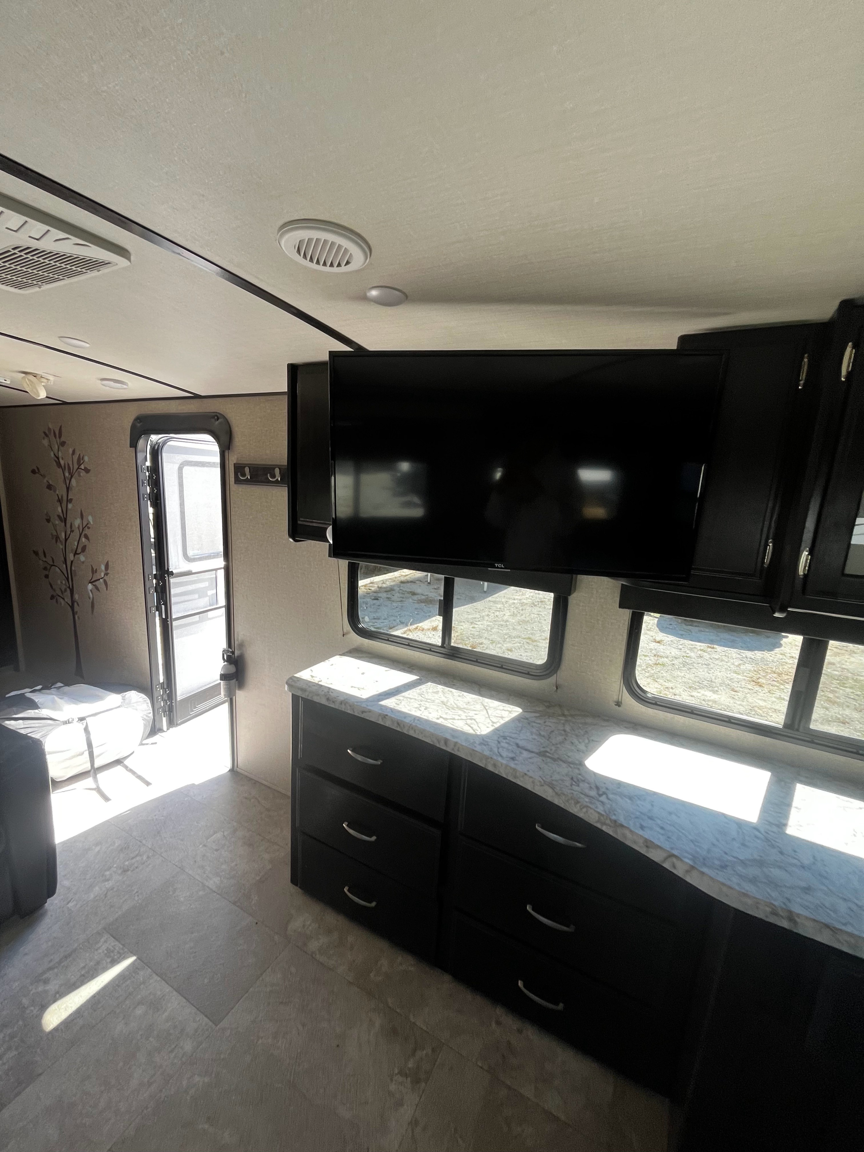 RV rental interior: living area with TV, spacious dresser, bright windows, and an open door to the outdoors.. Grand Design Imagine 2019