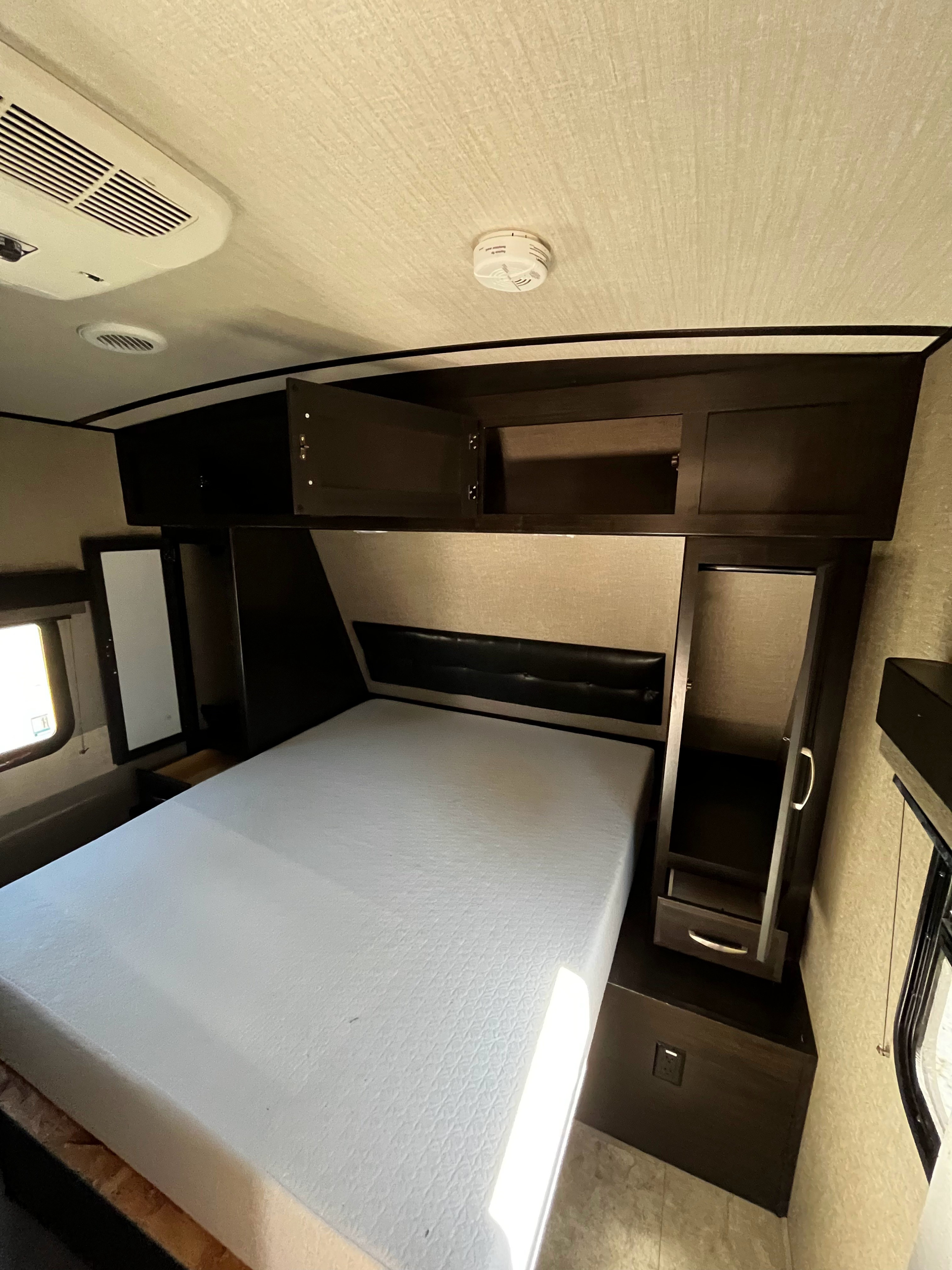 Comfortable RV rental bedroom featuring a large mattress, dark wood cabinetry, AC, and smoke detector.. Grand Design Imagine 2019