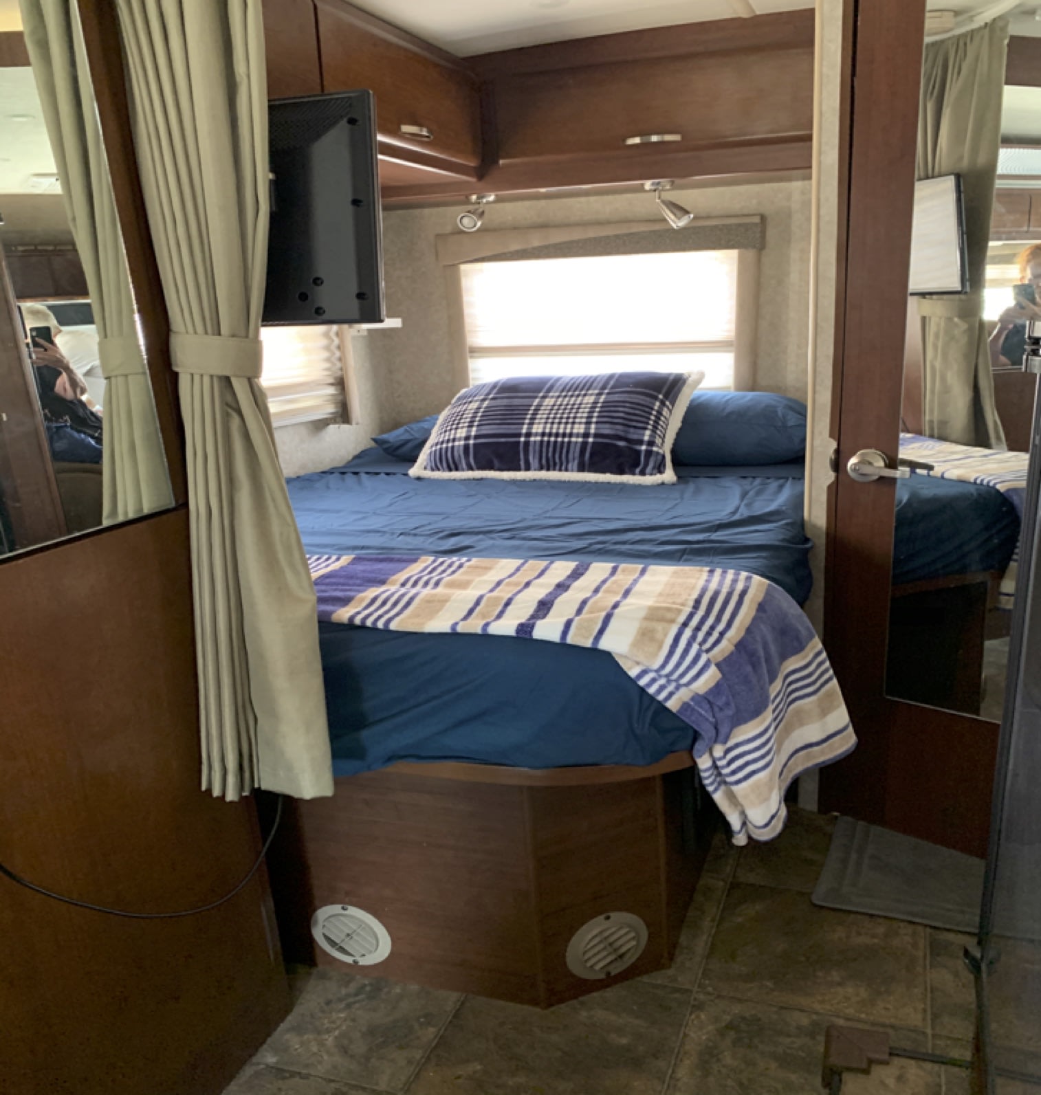 Compact RV rental bedroom with a bed, blue bedding, plaid pillow, striped blanket, TV, and window.. Fleetwood Tioga 2011