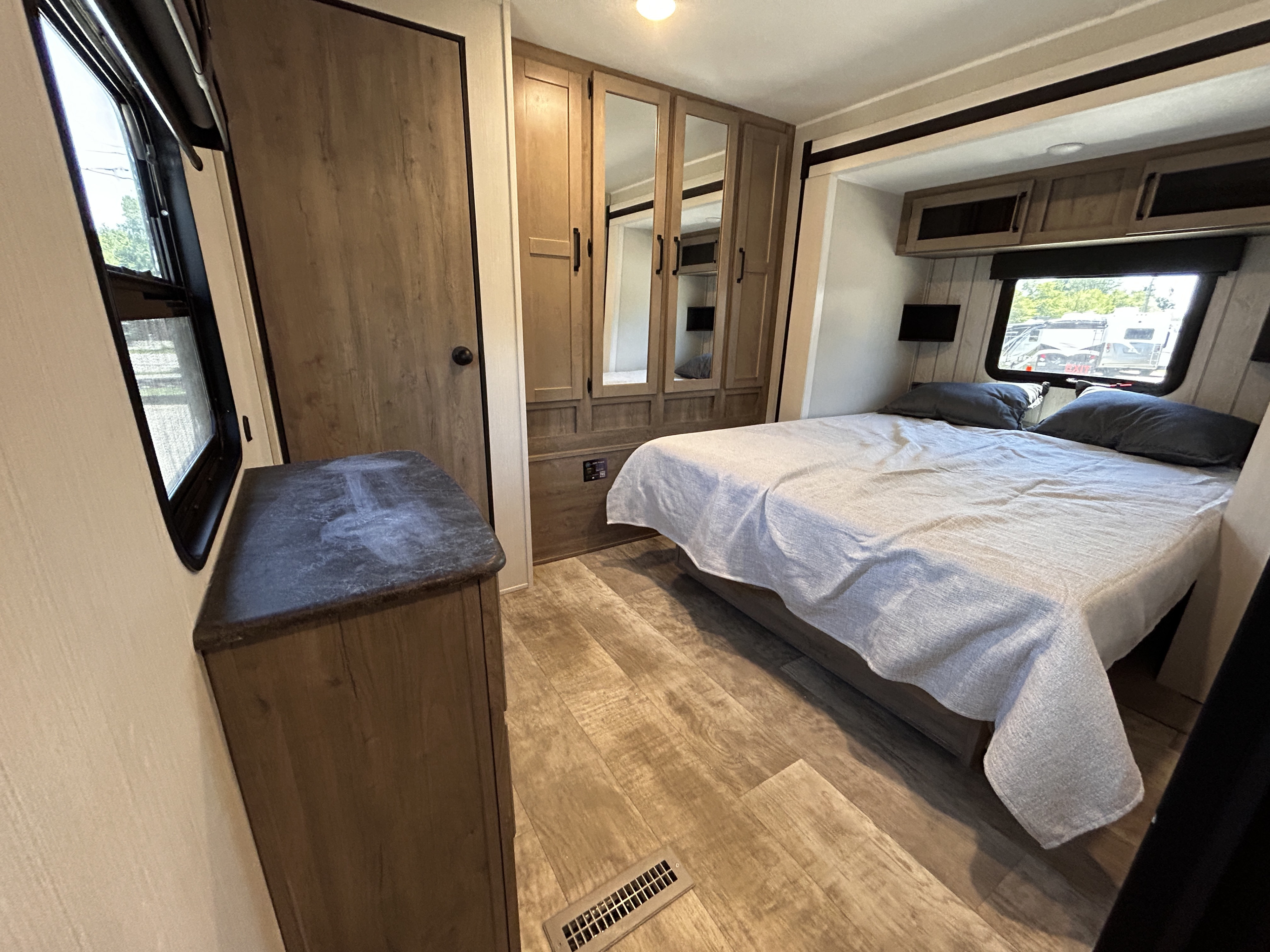 This RV rental bedroom features a bed with gray linens, a mirrored wardrobe, window, and wood-look flooring.. Palomino Puma 2025